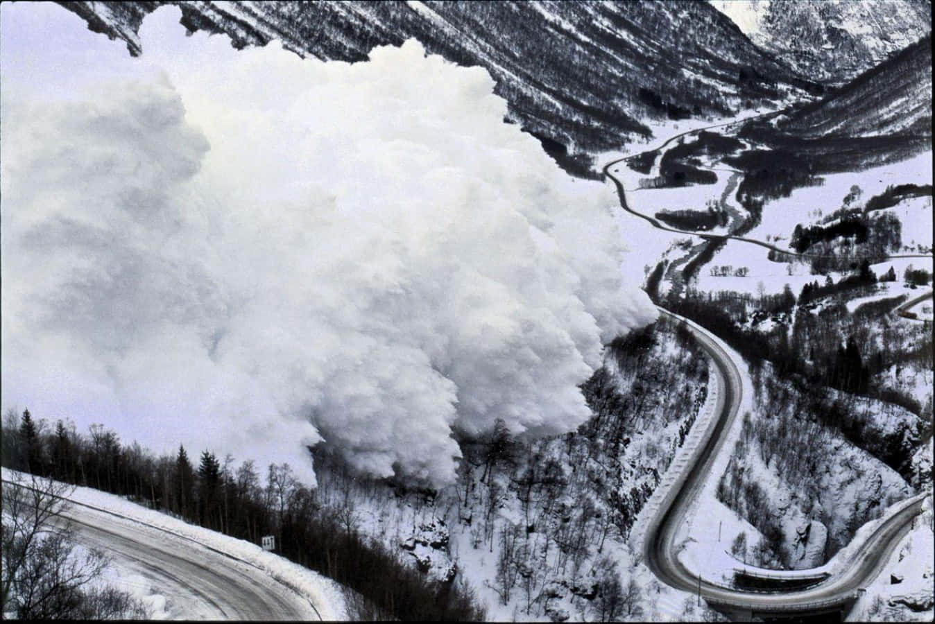 雪崩從山谷中傾瀉而下，掩埋了一條蜿蜒的道路。