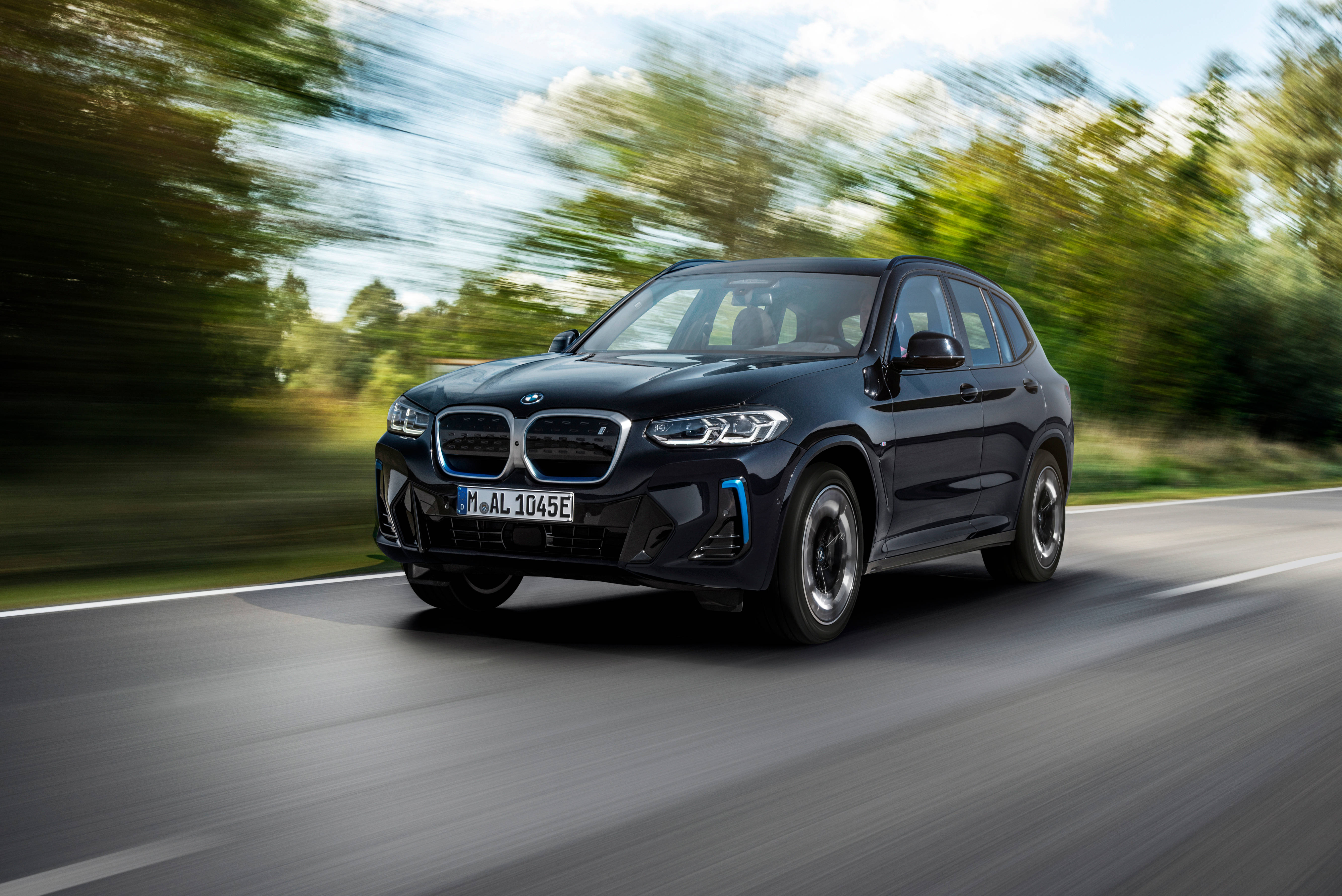 自然男孩黑色BMW 壁紙 — 一輛時尚的黑色寶馬電動SUV在陽光明媚的道路上飛馳，模糊的綠色樹木從旁掠過。