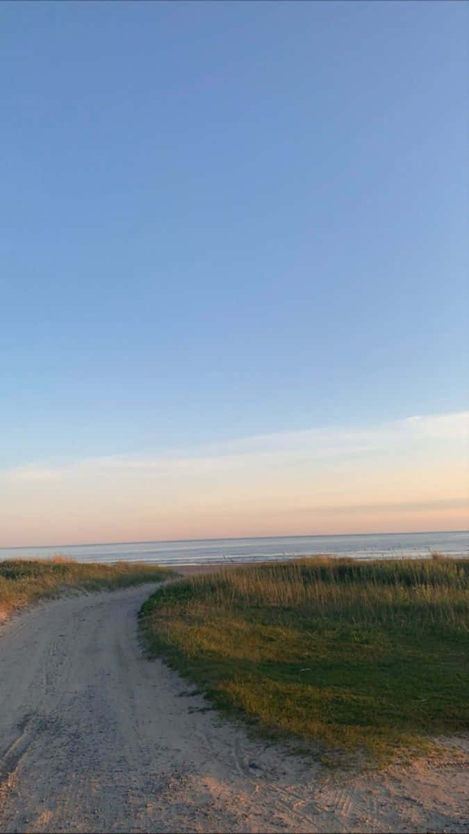 蜿蜒的泥土小徑穿過長滿草的沙丘，在日落時分通向海洋。