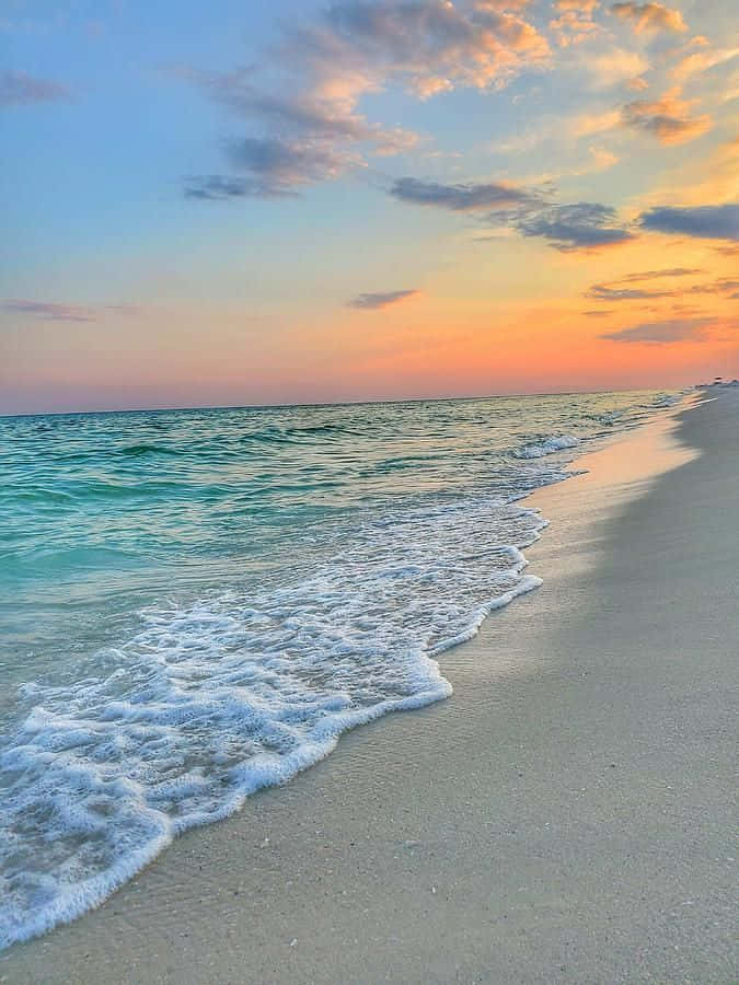 夕陽下的海浪輕輕湧上沙灘，天空色彩繽紛。