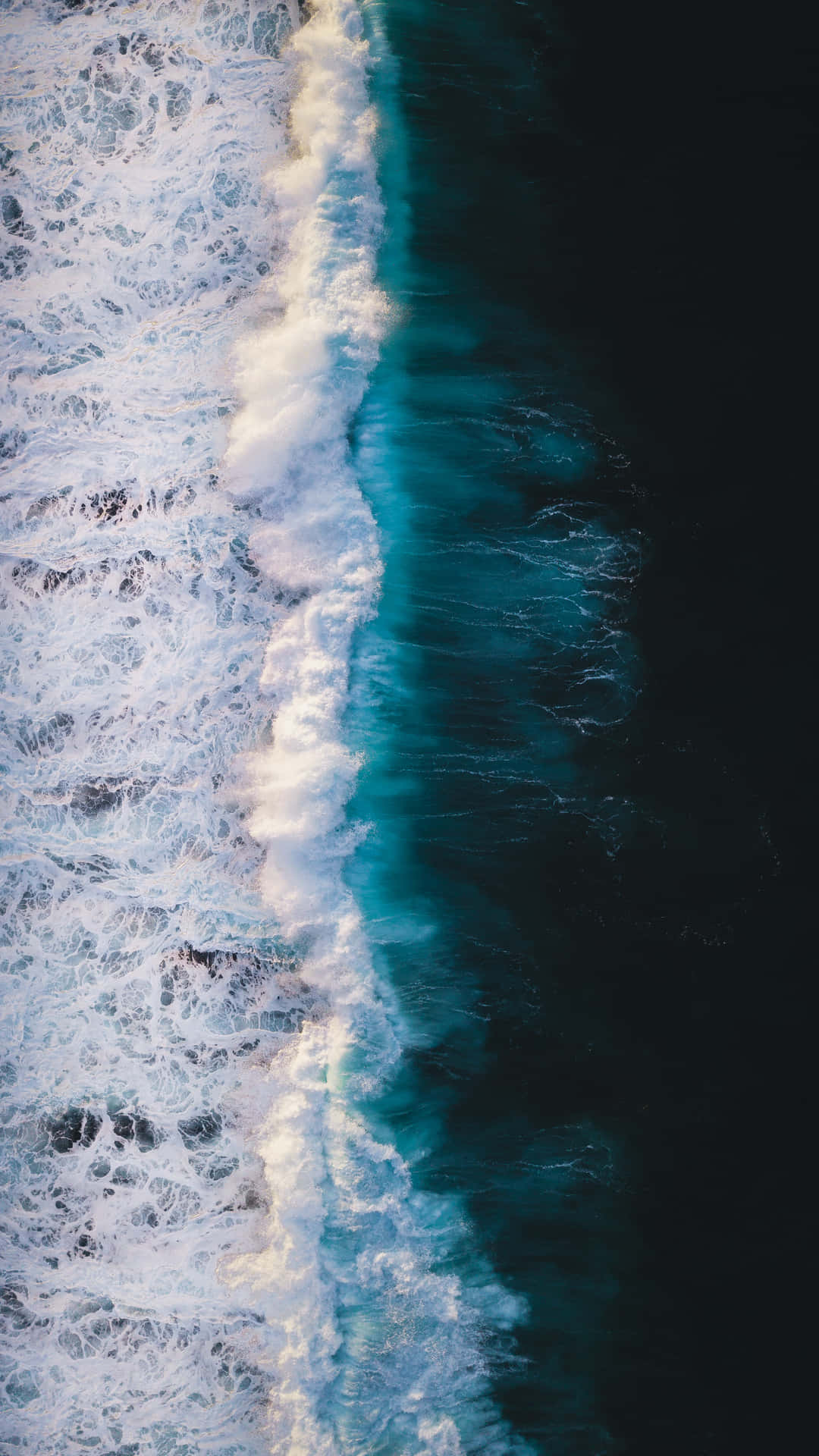 從高空拍攝海浪拍打，在深藍色海水中形成白色泡沫。