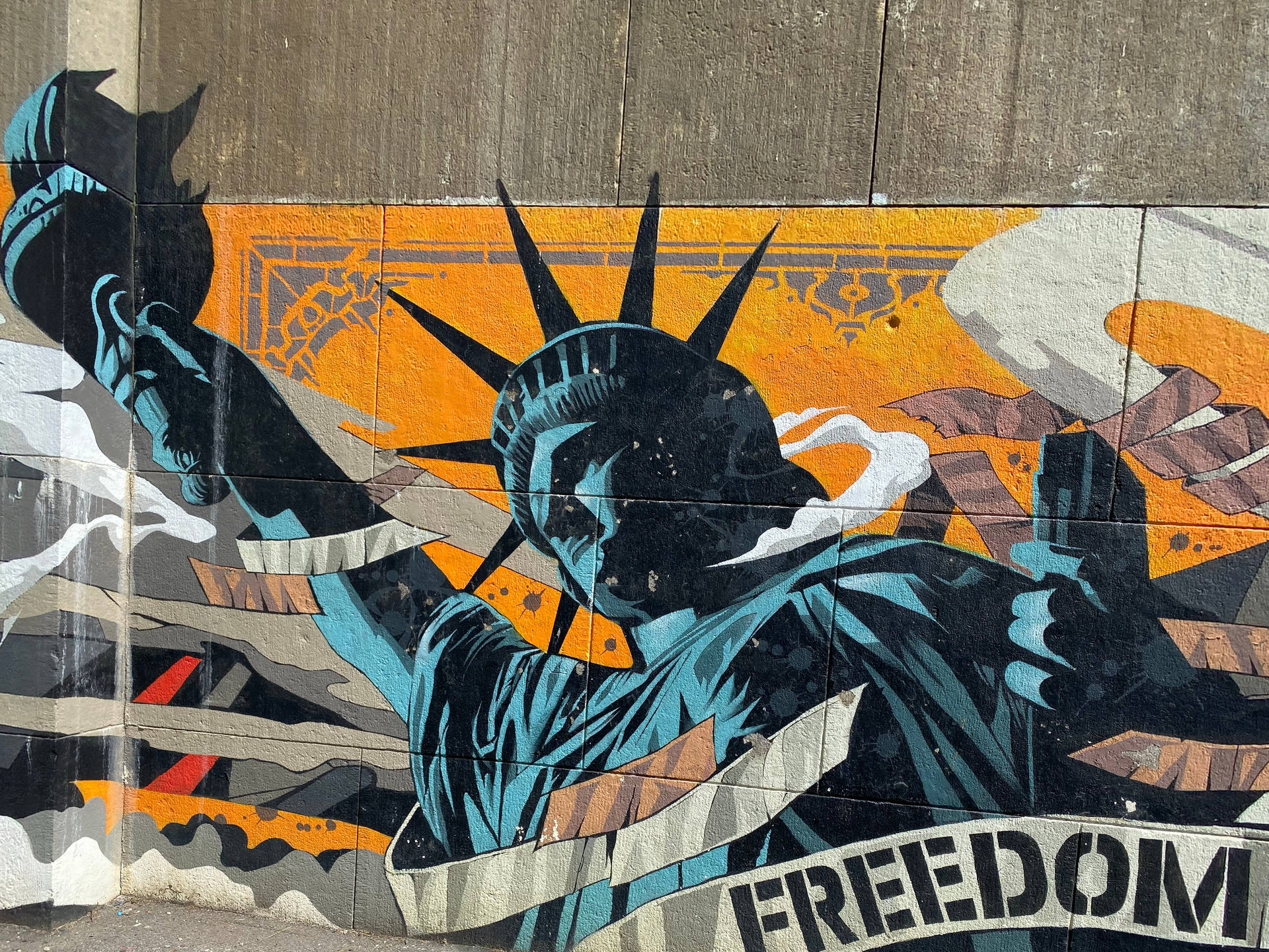 塗鴉壁畫，描繪自由女神像手持火炬和刻有「FREEDOM」橫幅的石板，位於混凝土牆上。