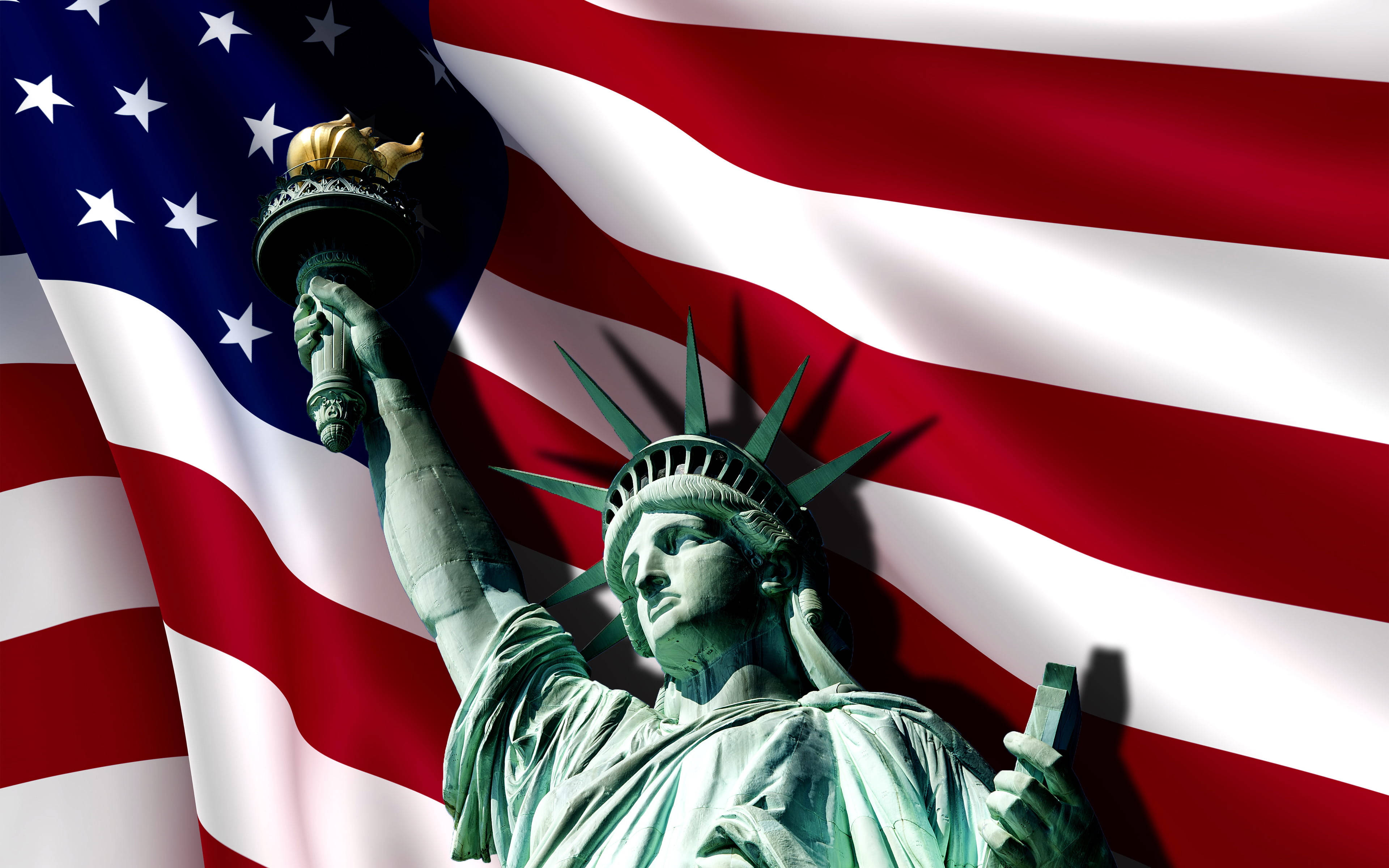 new york 4K 桌布 壁紙 — 自由女神像高舉火炬，驕傲地站立在飄揚的美國國旗前，國旗上有大膽的紅、白、藍條紋。