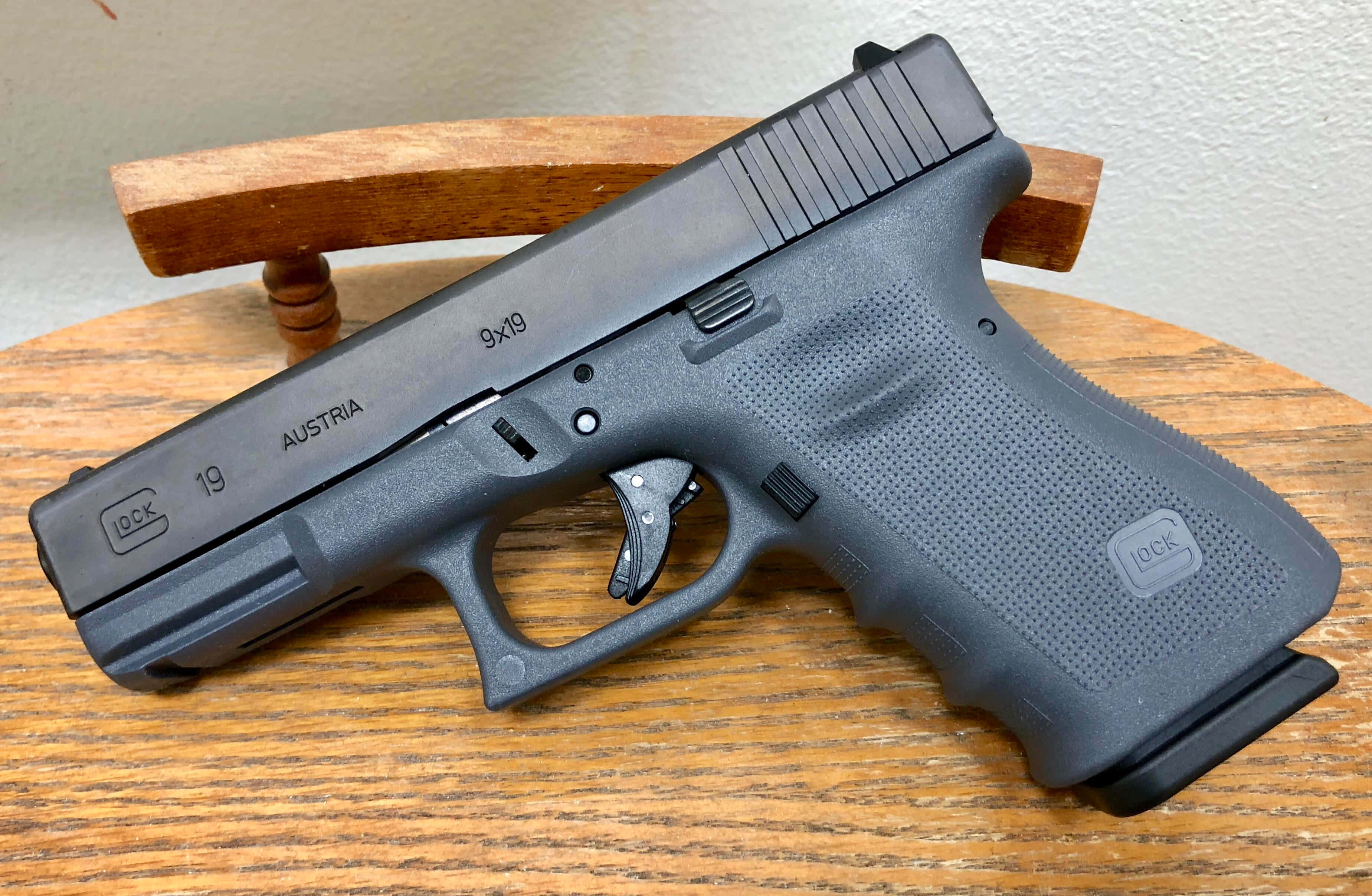 自衛與居家防衛之選：Glock 19 壁紙 — 一把黑色Glock 19手槍放在木桌上，帶有紋理握把和可見標記。