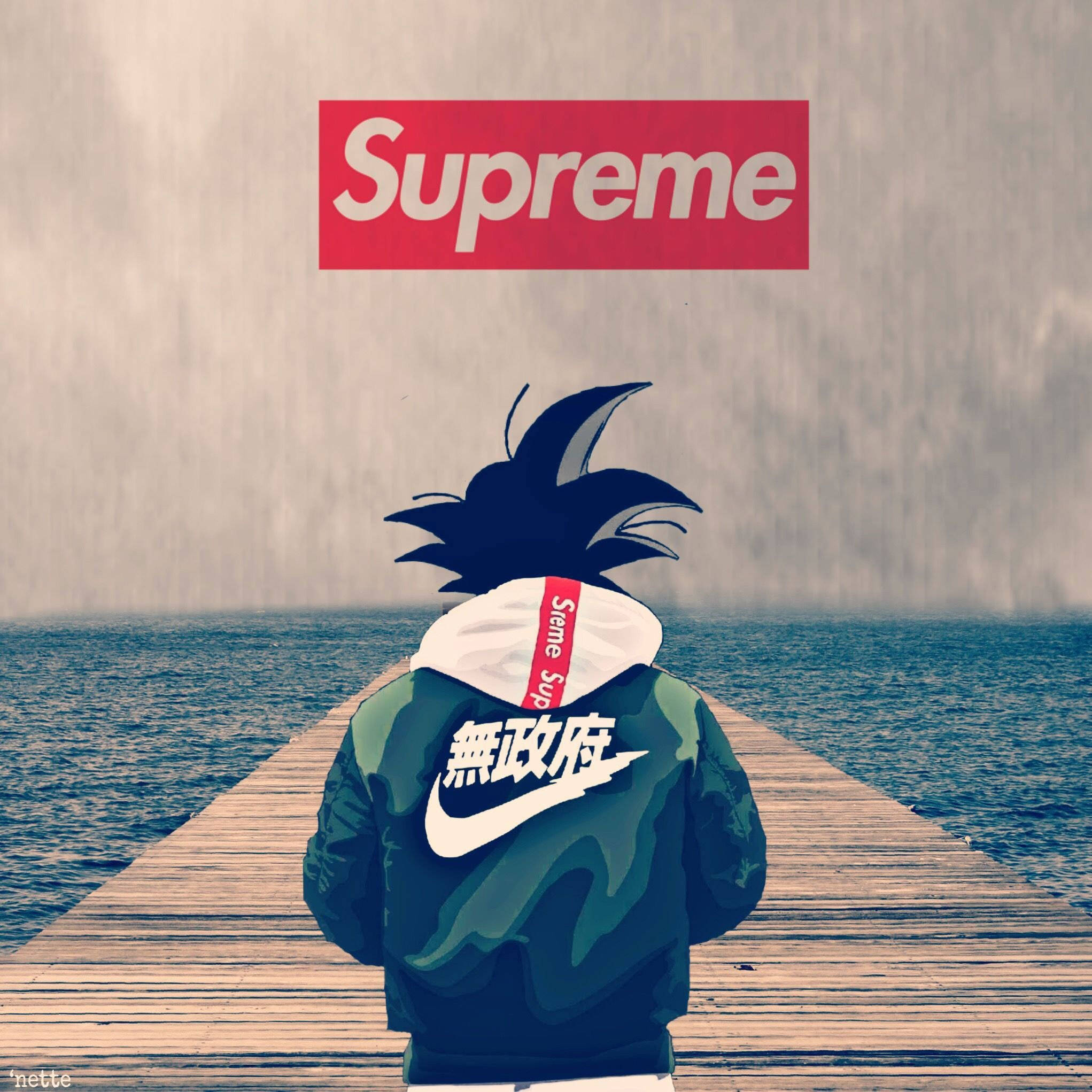 至尊悟空穿Supreme與Nike 壁紙 — 一個風格化的動漫角色，有著尖刺頭髮，站在木製碼頭上，面對著灰色天空下的廣闊海洋，上方漂浮著一個紅色的Supreme標誌。