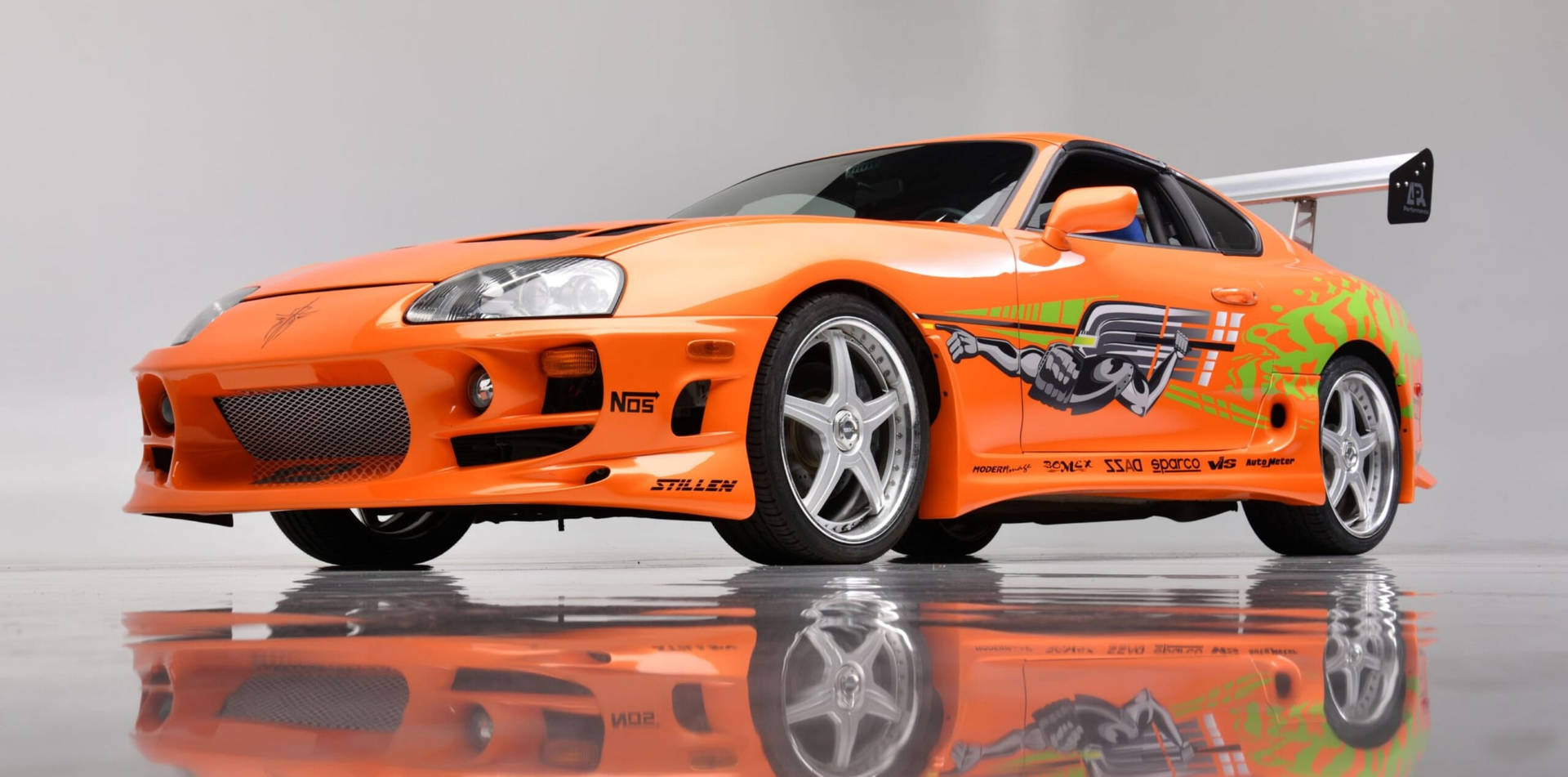 橙色豐田Supra，帶有賽車貼紙和後翼，在反射地板上。