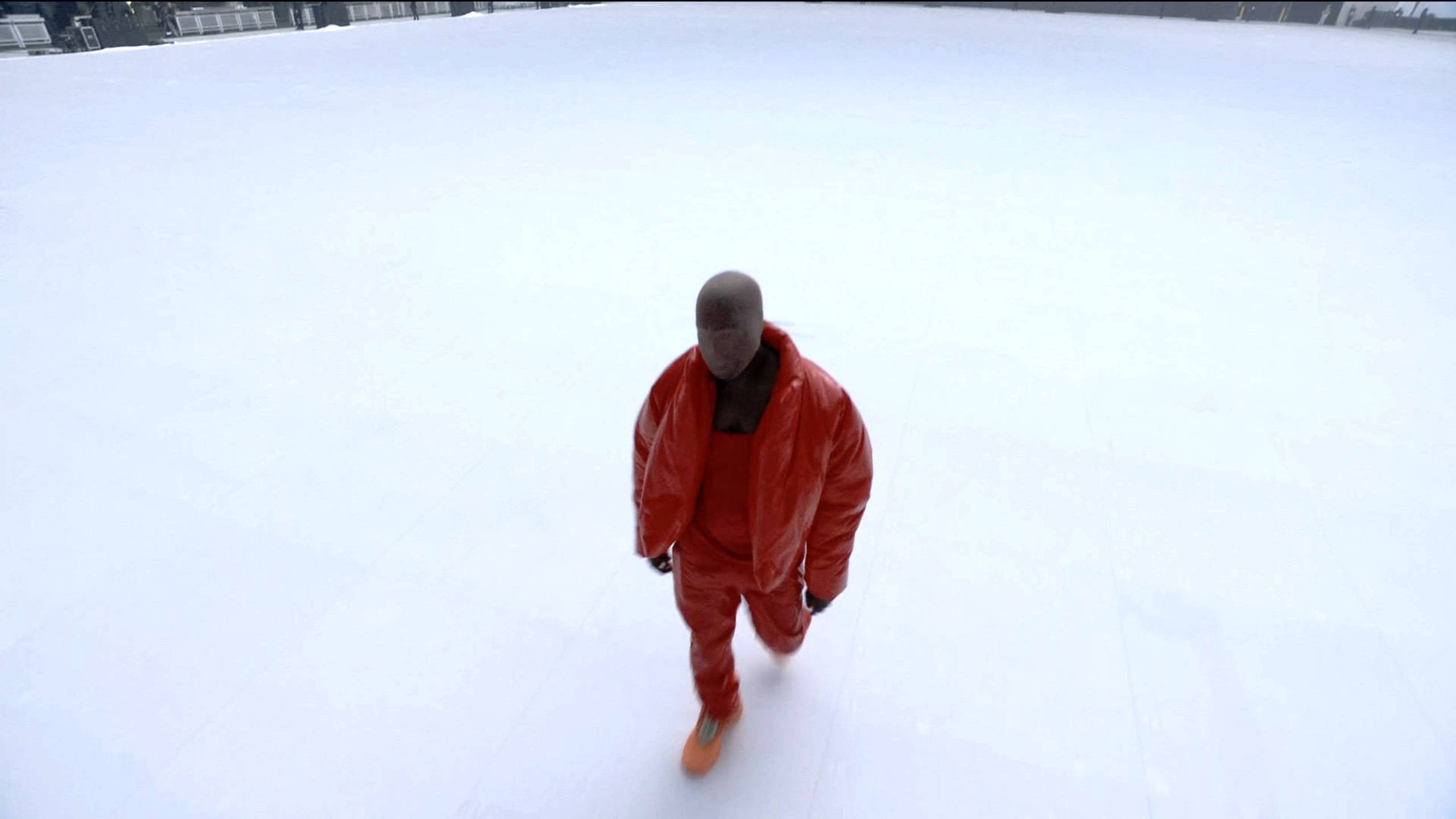 致敬坎耶母親 Donda West 的傳奇 壁紙 — 一名身穿亮紅色雪衣的男子在陰天之下獨自走過廣闊的雪地。