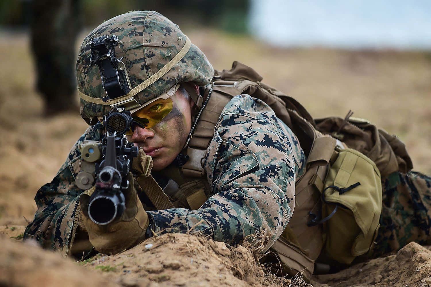 穿著迷彩裝備的士兵在泥地上以俯臥姿勢瞄準步槍。