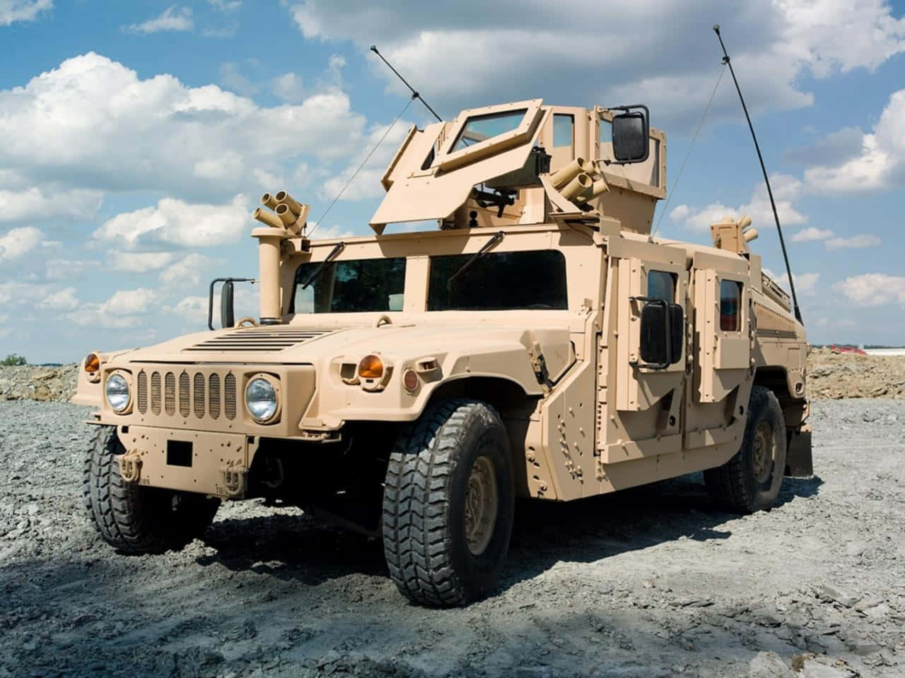 軍用沙色悍馬車配備武器，在岩石地形上，藍天白雲。