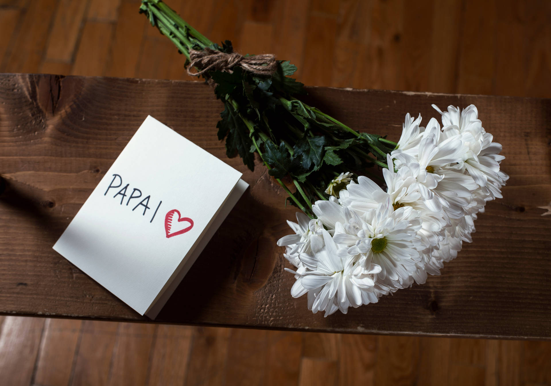 寫有「PAPAI」和心形的便條，旁邊有白色花，在木上。