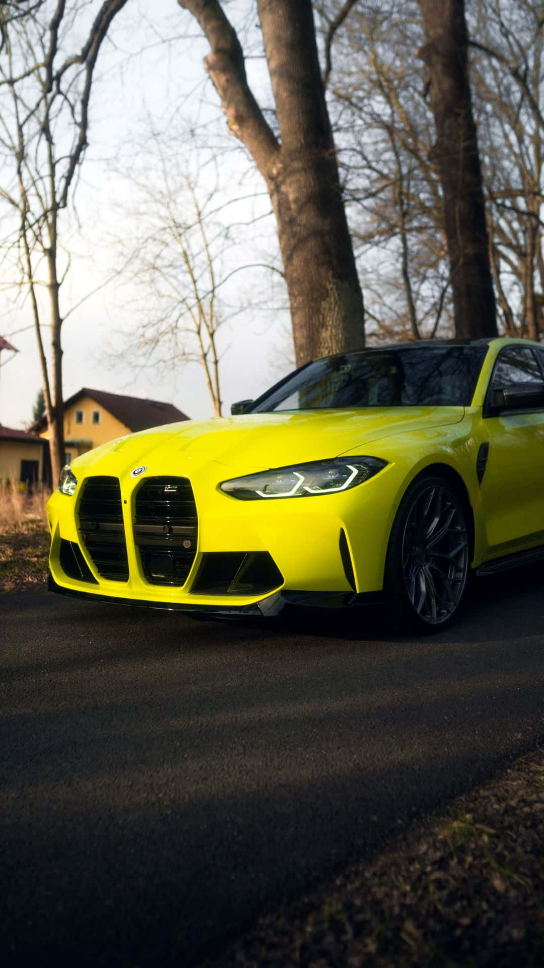 與 Android BMW 一同感受開闊道路的自由 壁紙 — 一輛充滿活力的黃色BMW M3跑車停泊在黃昏時分的林蔭大道上，樹枝光禿，環境光線柔和。