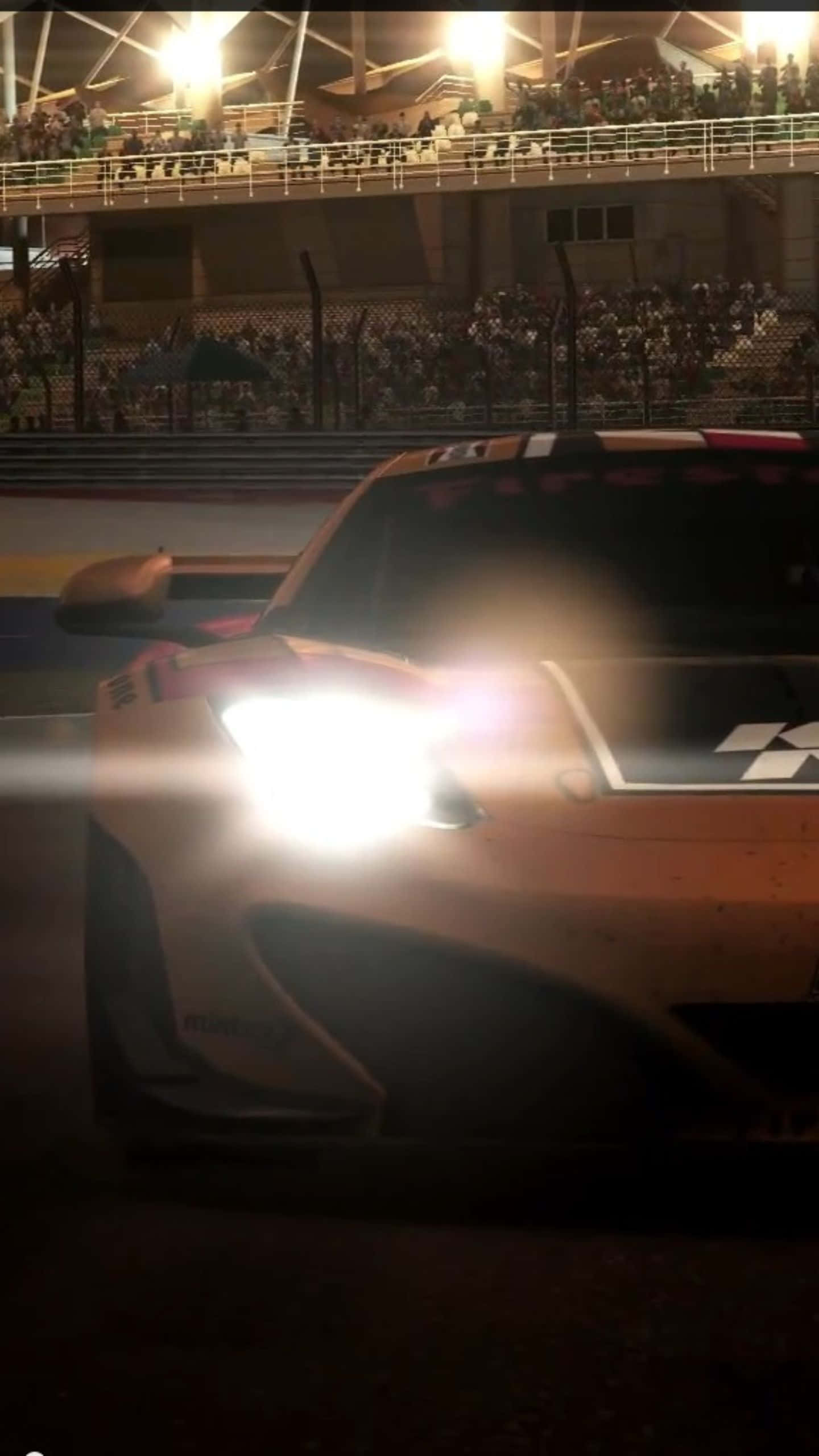 與 Android Grid Autosport 一起衝向勝利 壁紙 — 一輛發光的橙色賽車的頭燈劃破夜空，在體育場賽道上飛馳而過，周圍是歡呼的人群。