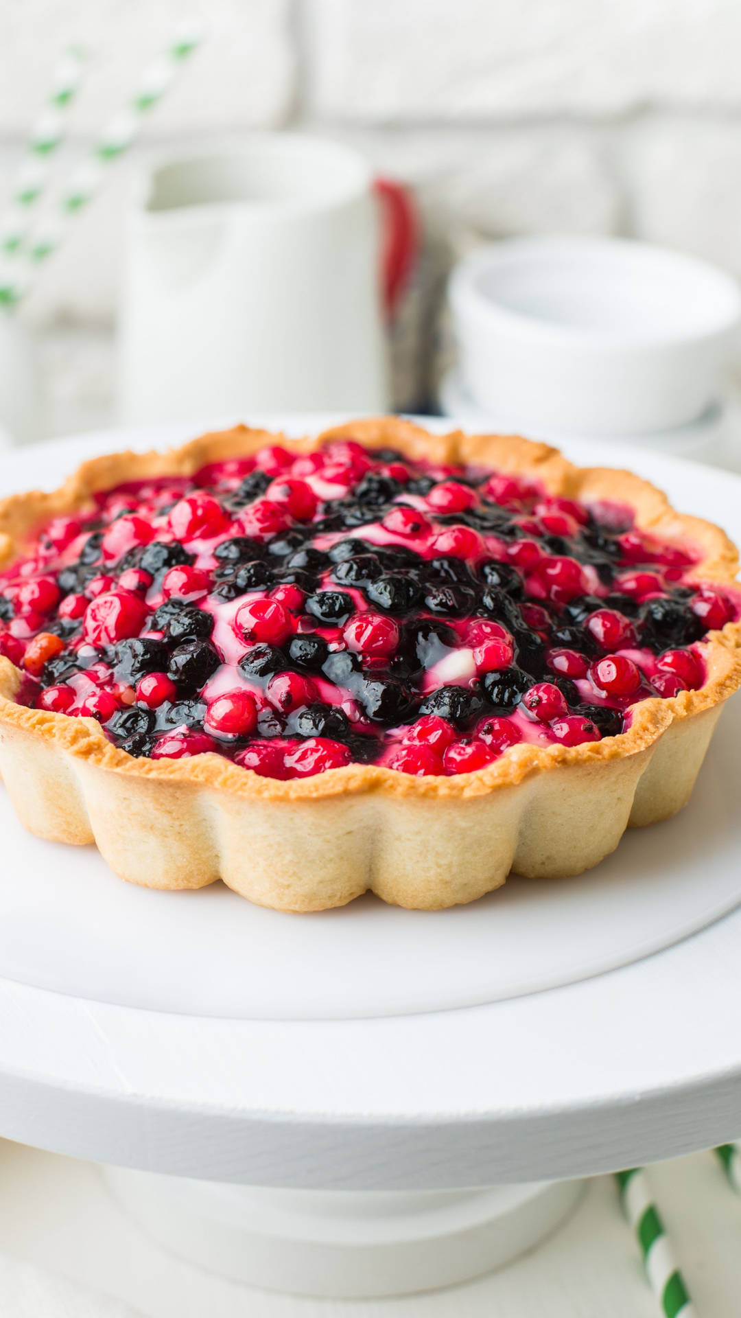 一個莓果撻放在白色蛋糕架上，背景是白色磚牆。