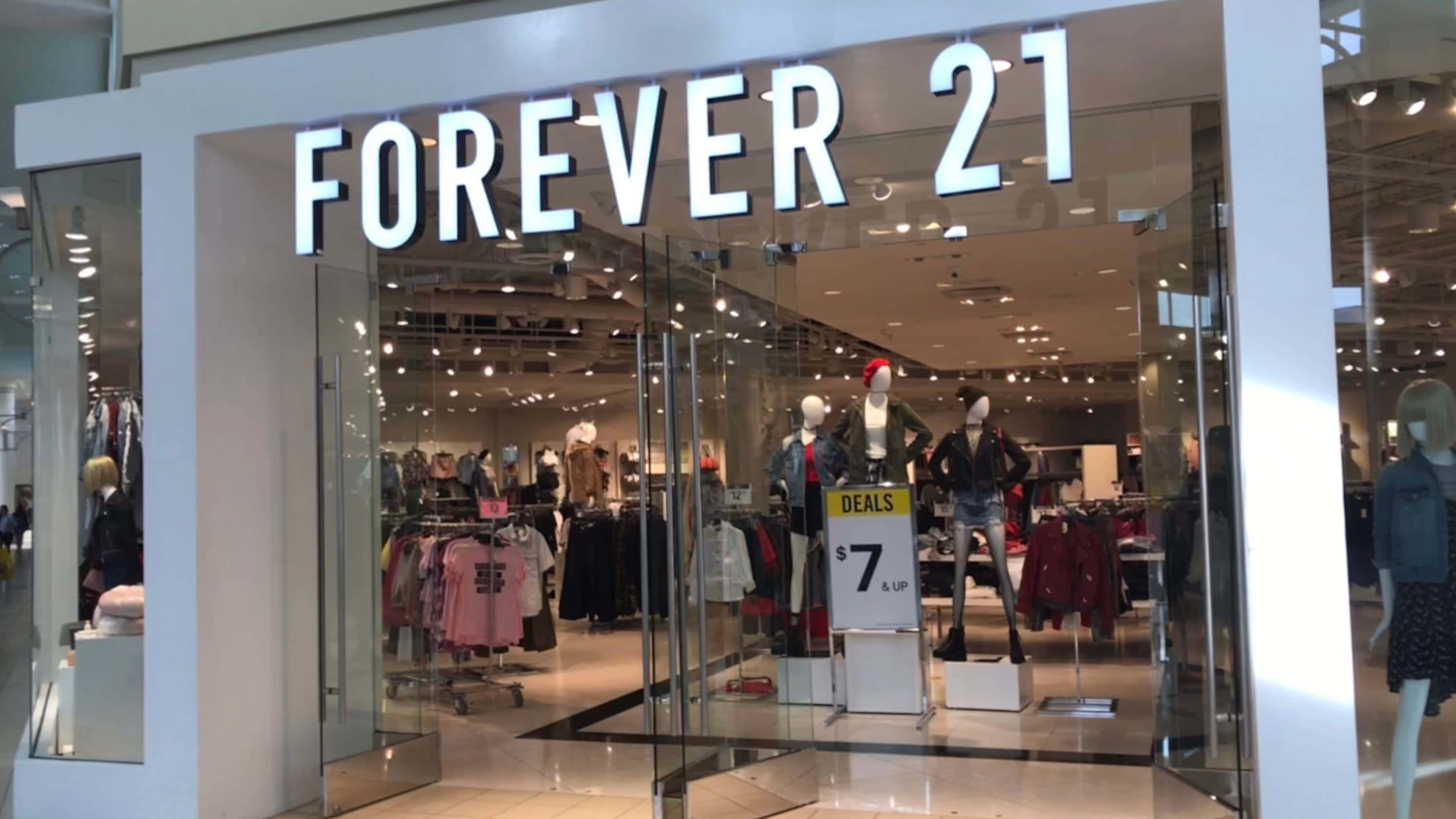 與 Forever 21 一起迎接夏日時尚 壁紙 — 光線明亮的Forever 21店舖正面，設有玻璃門、人體模型和展示色彩繽紛衣物的貨架。