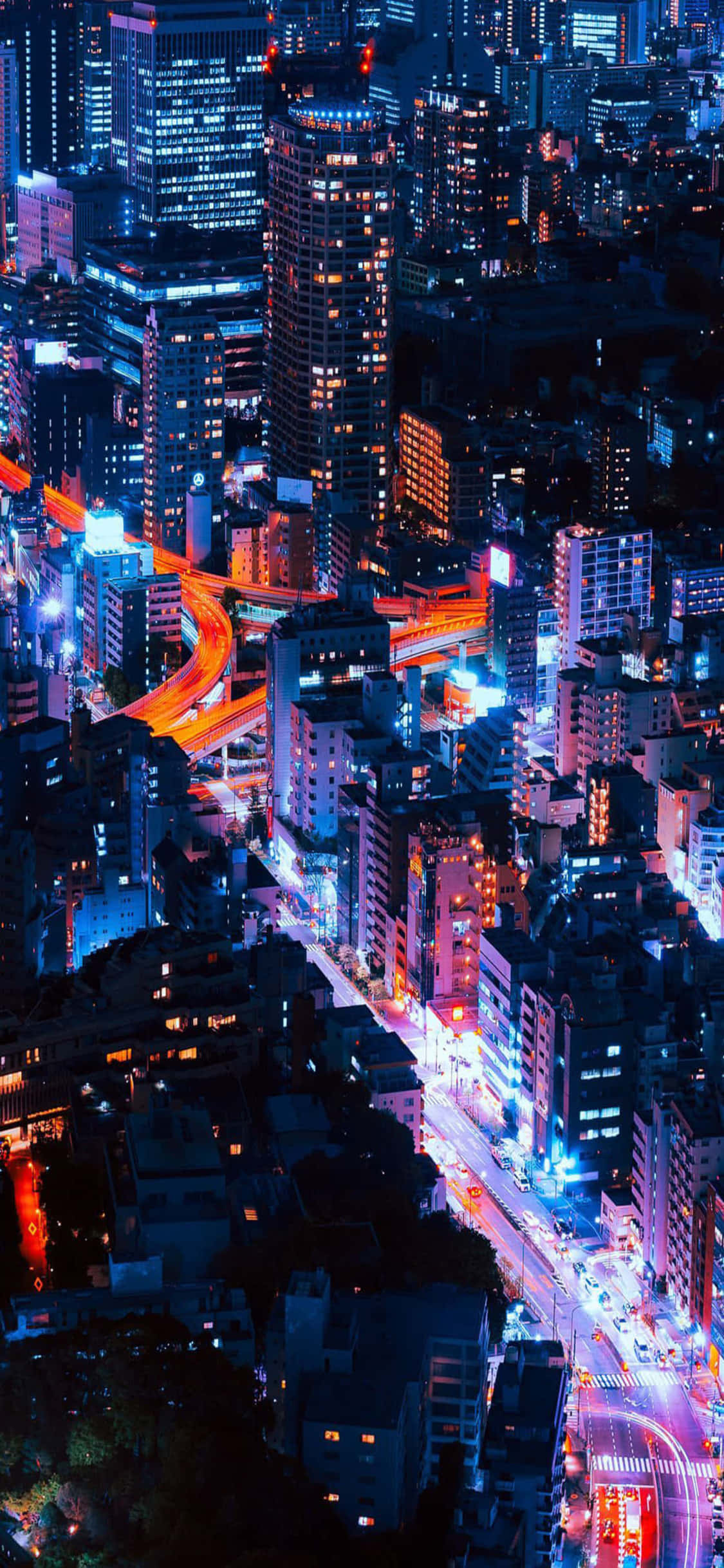 與 iPhone X 一同欣賞加州日落 壁紙 — 夜晚霓虹燈照亮的天際線航拍圖，閃爍的摩天大樓和鮮豔的車流軌跡。