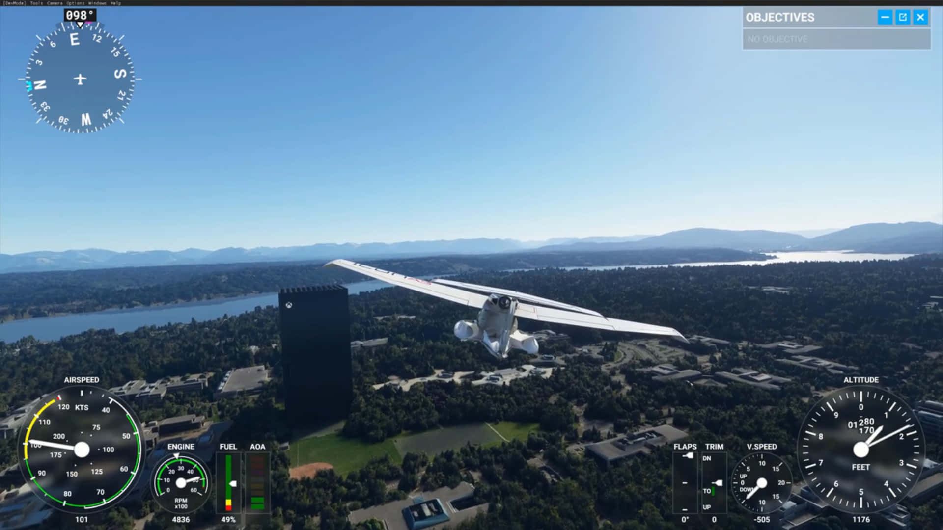 與 Microsoft Flight Simulator 一同探索天空 壁紙 — 一架白色單引擎飛機在晴朗藍天下，低飛過陽光明媚的郊區景觀，有河流和遠處的山脈。