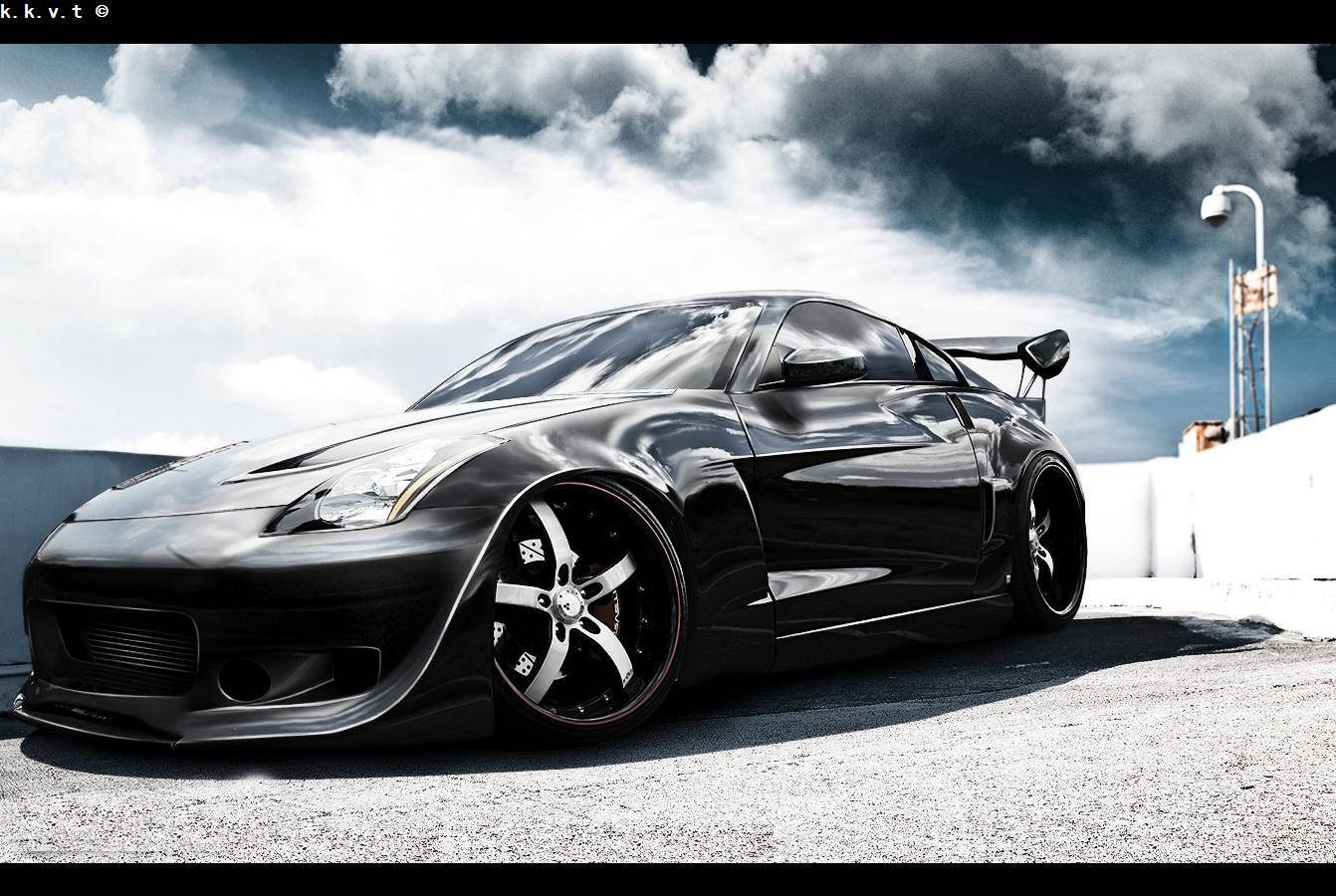 與 Nissan 350z 一同感受速度 壁紙 — 一輛光澤黑色改裝跑車，配備寬體套件和大輪圈，停在戲劇性多雲天空下的瀝青路面上。