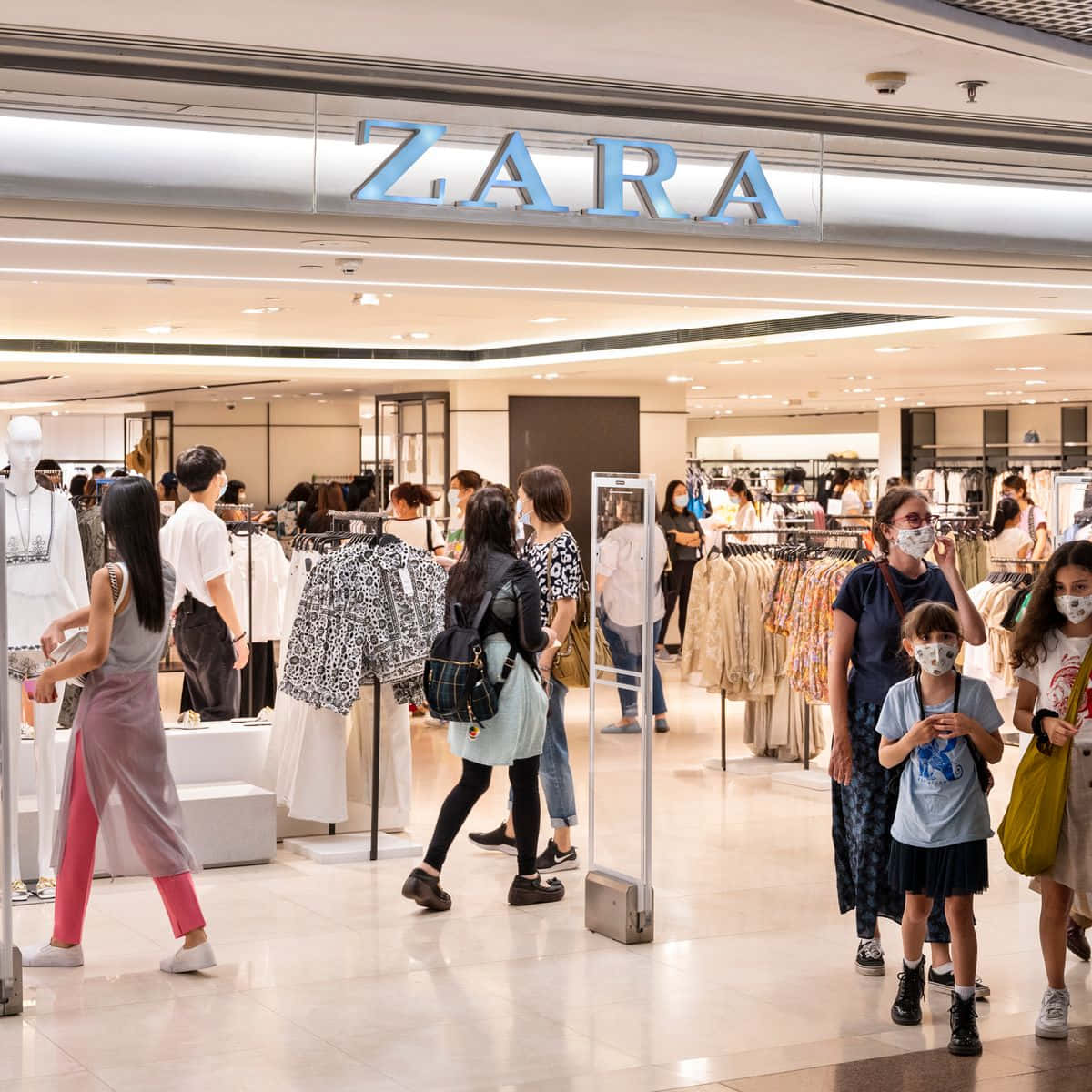 與 Zara 保持時尚與潮流 壁紙 — 購物者在光線充足的Zara店內瀏覽衣架，店鋪採用現代簡約設計和反光地板。