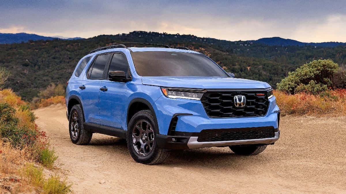 與2023 Honda Pilot 一同享受極致公路冒險 壁紙 — 一輛充滿活力的藍色本田SUV在陰天下的塵土飛揚的山路上自信地行駛。