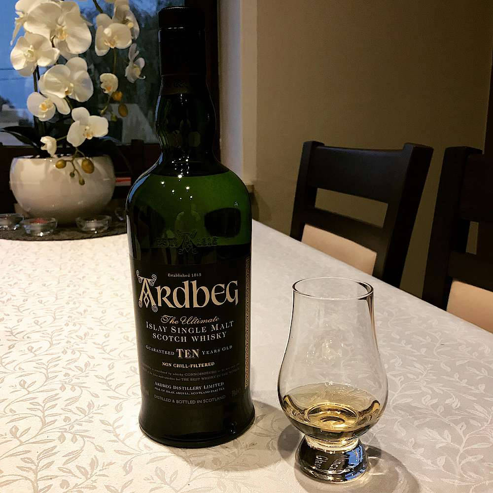 一瓶Ardbeg威士忌和品酒杯放在圖案桌布上，配有白色蘭花。