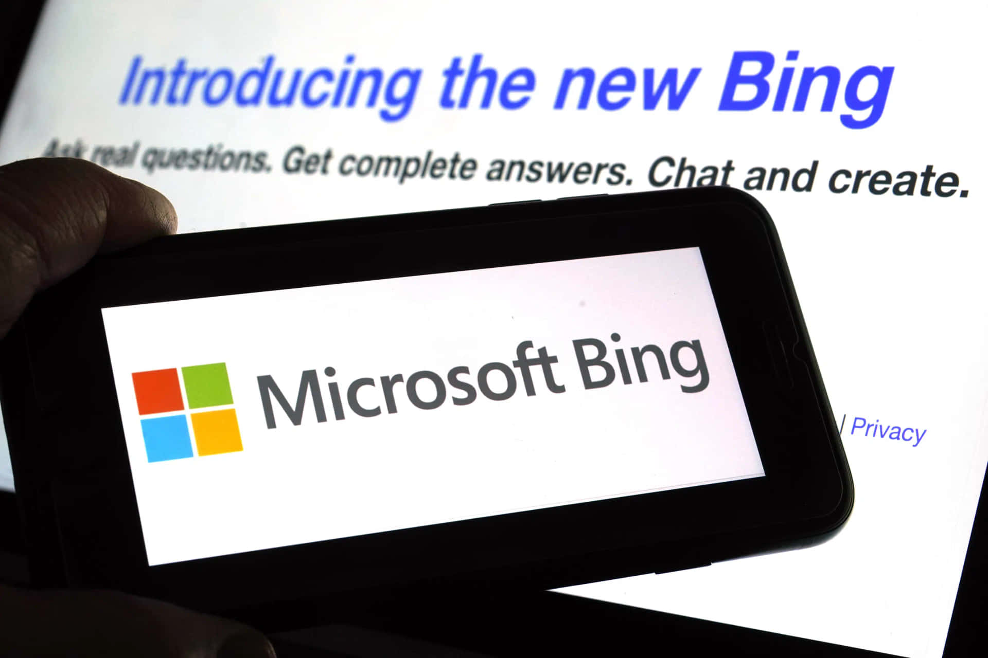 手拿著顯示Microsoft Bing標誌的電話，背景有筆記型電腦。