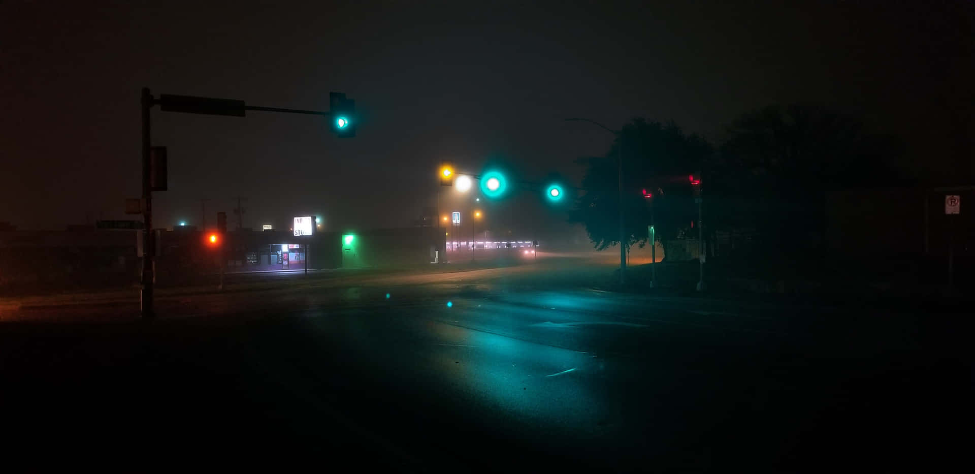霧氣瀰漫的夜晚街道，發光的交通燈在濕漉漉的路面上反射。