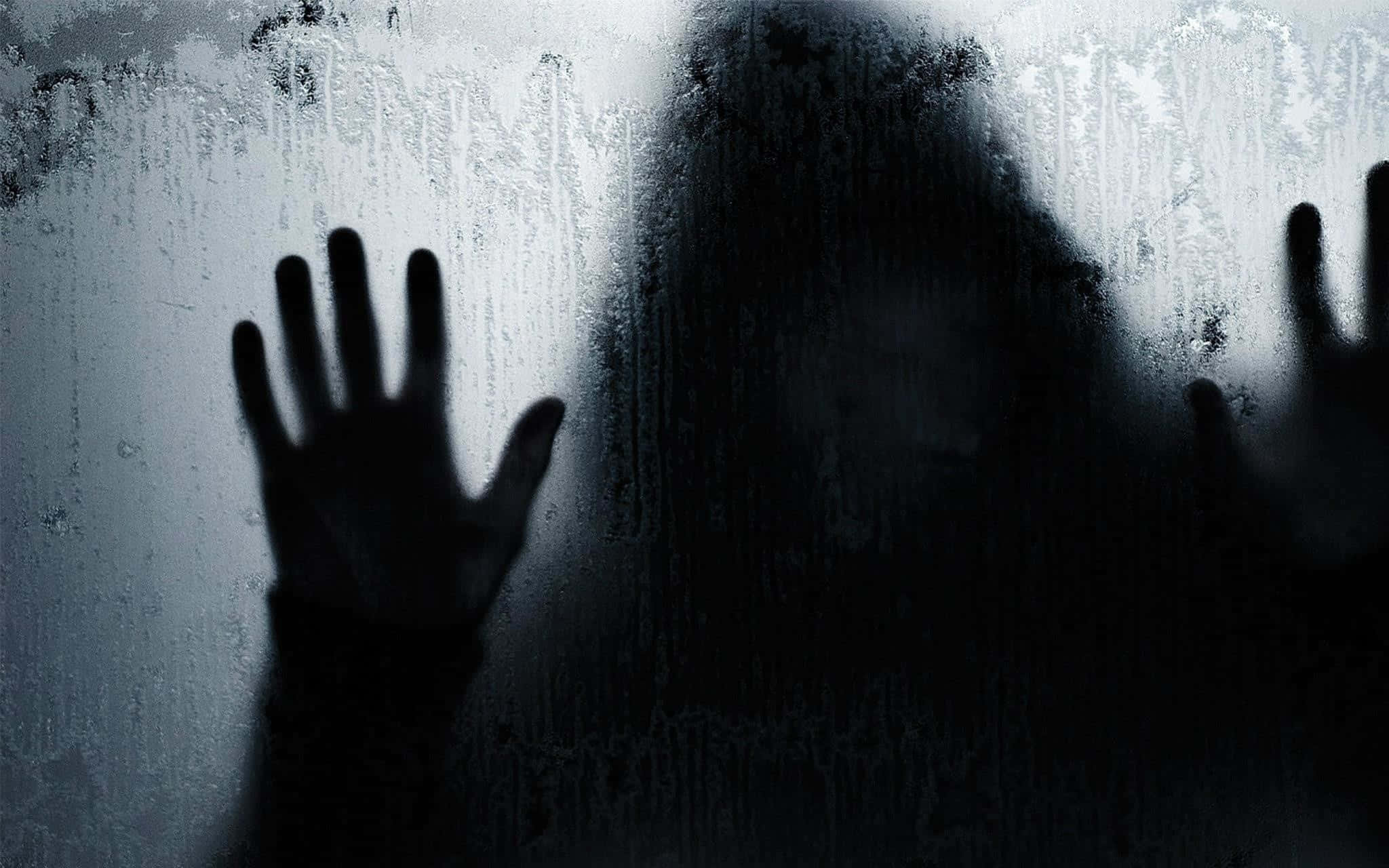 與Ghost探索超自然世界 壁紙 — 一個陰暗的身影將雙手按在結霜的窗戶上，場景陰森寒冷。