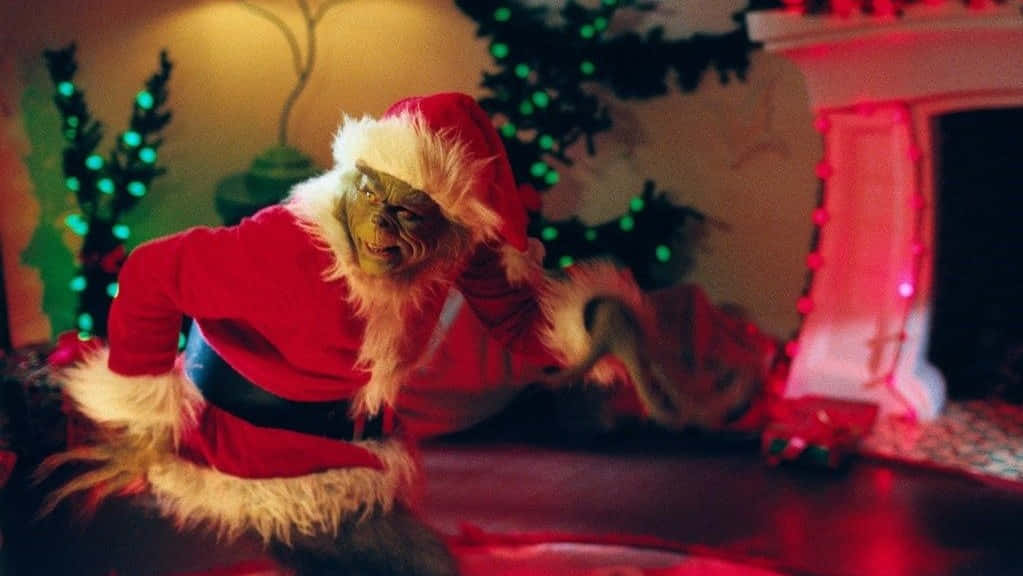與Grinch一起「Zoom」度過假日！ 壁紙 — 身穿紅色聖誕老人服裝的鬼靈精蹲在一個裝飾著發光綠色和紅色燈光的壁爐旁。