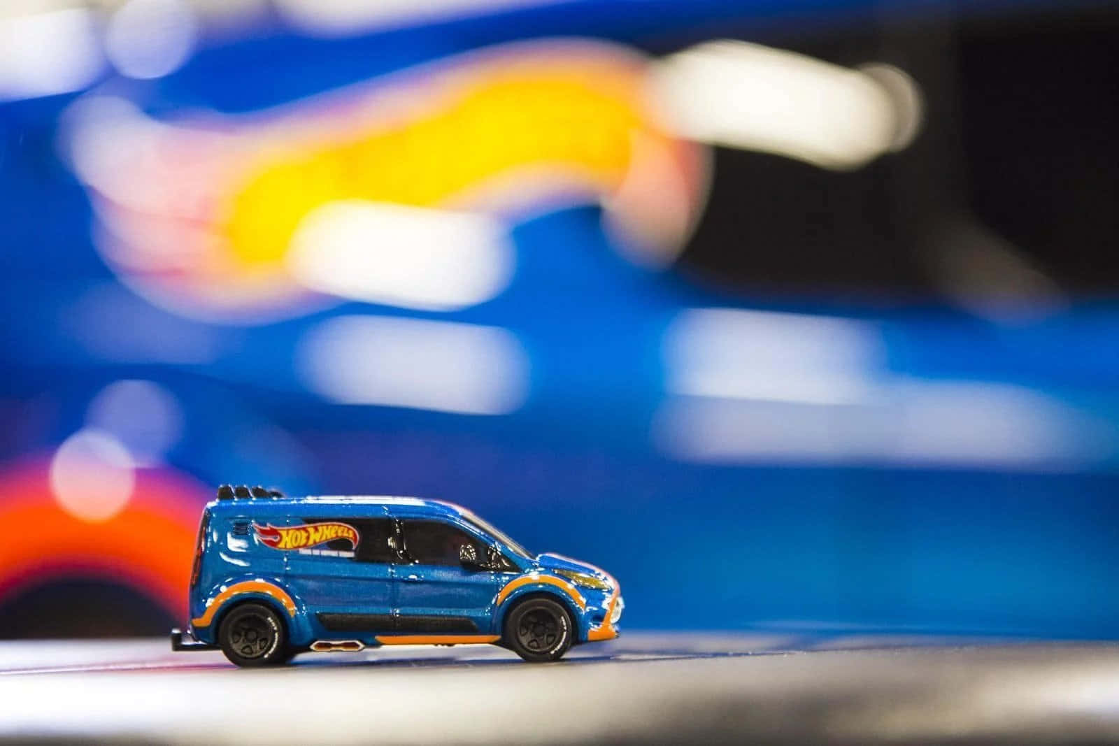 藍色 Hot Wheels 玩具貨車帶有橙色飾邊，背景模糊多彩。