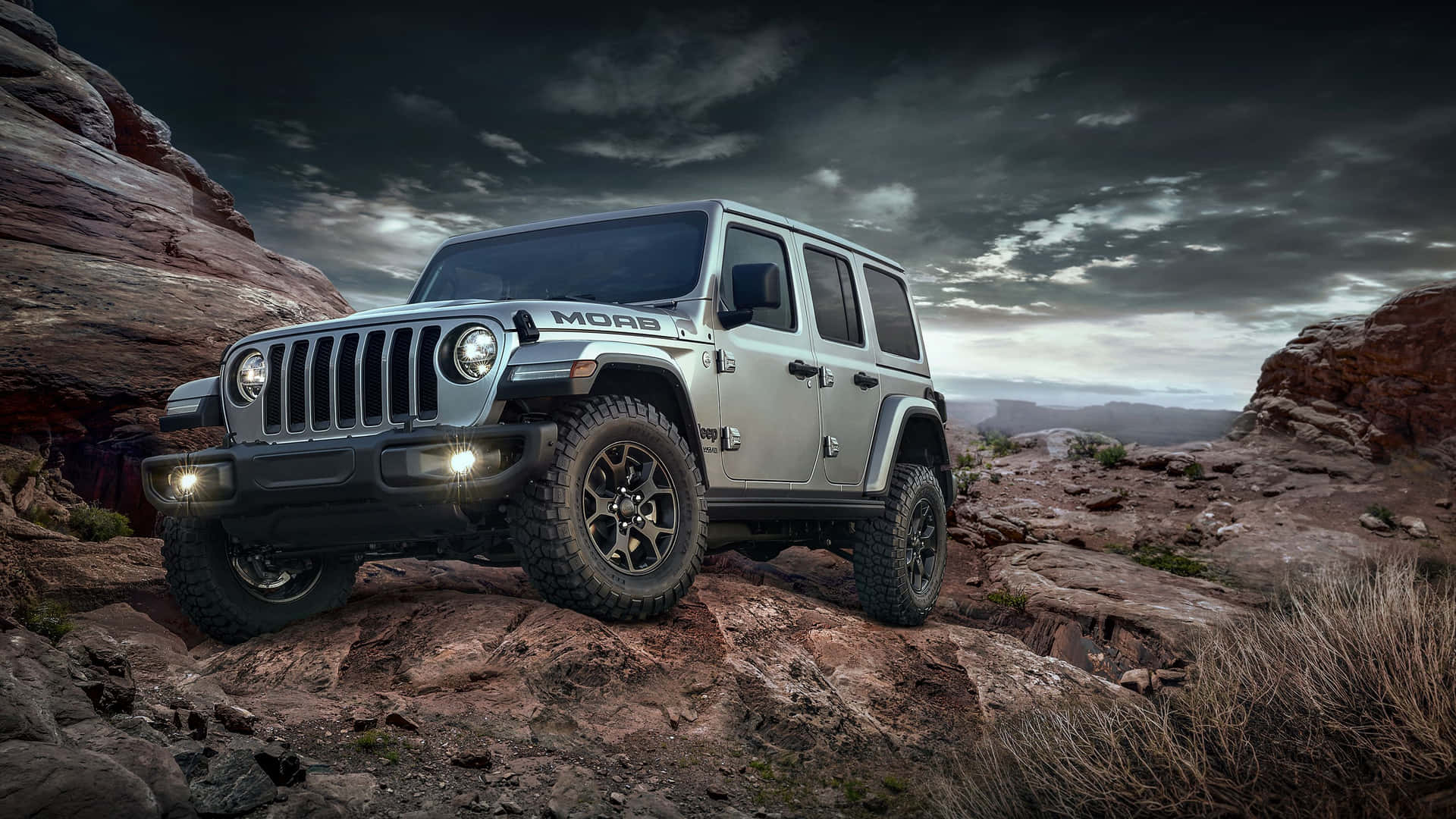 銀色Jeep Wrangler在暴風雨天空下穿越岩石沙漠地形。