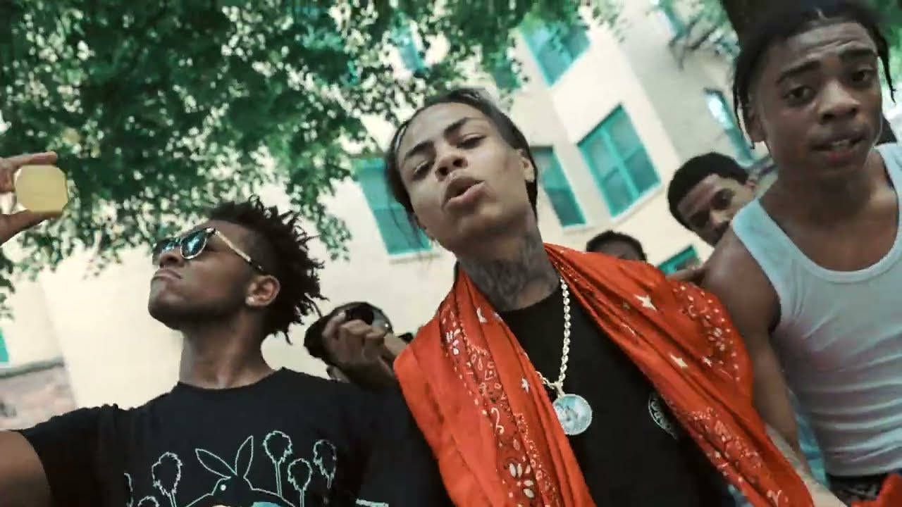 年輕男子在戶外擺姿勢，其中一人手持金幣，靠近一棟建築物。