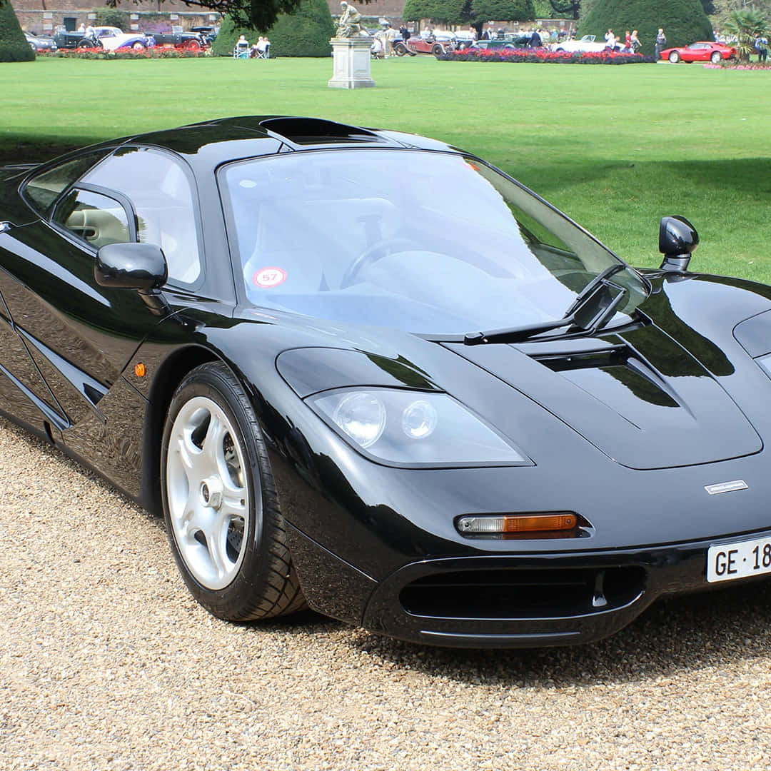 黑色McLaren F1超級跑車停放在公園環境中的碎石上。