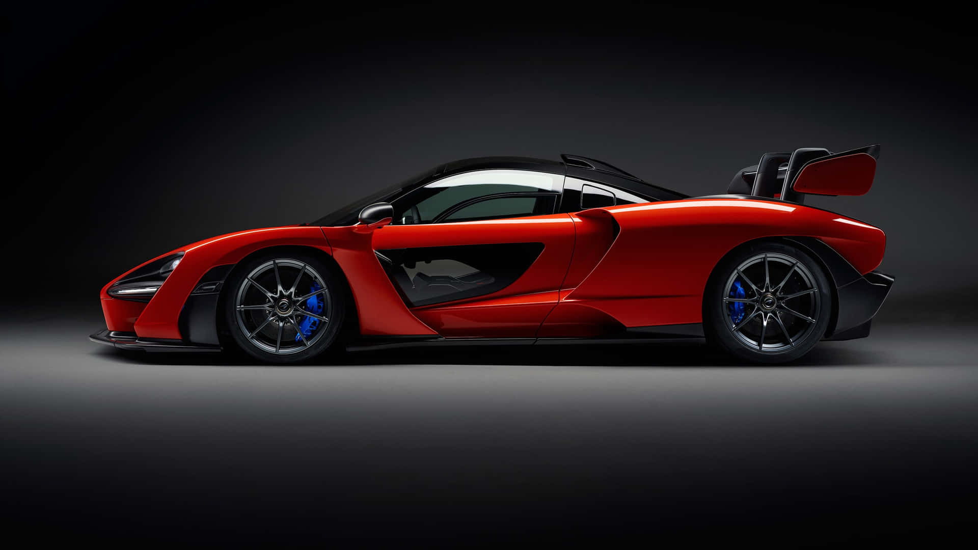在攝影棚燈光下，帶有黑色飾件和藍色制動器的紅色McLaren Senna跑車。