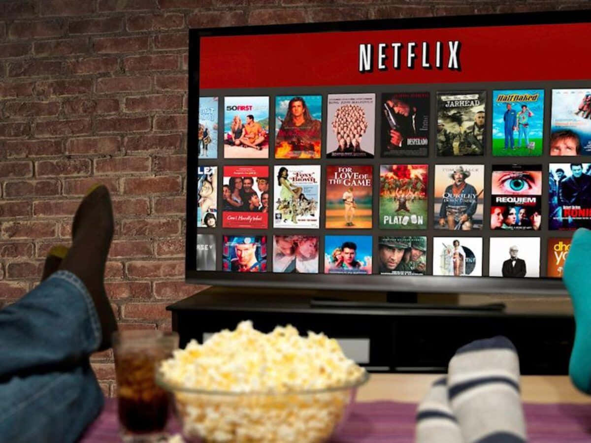 雙腳抬起，前面有爆米花和汽水，電視顯示Netflix。