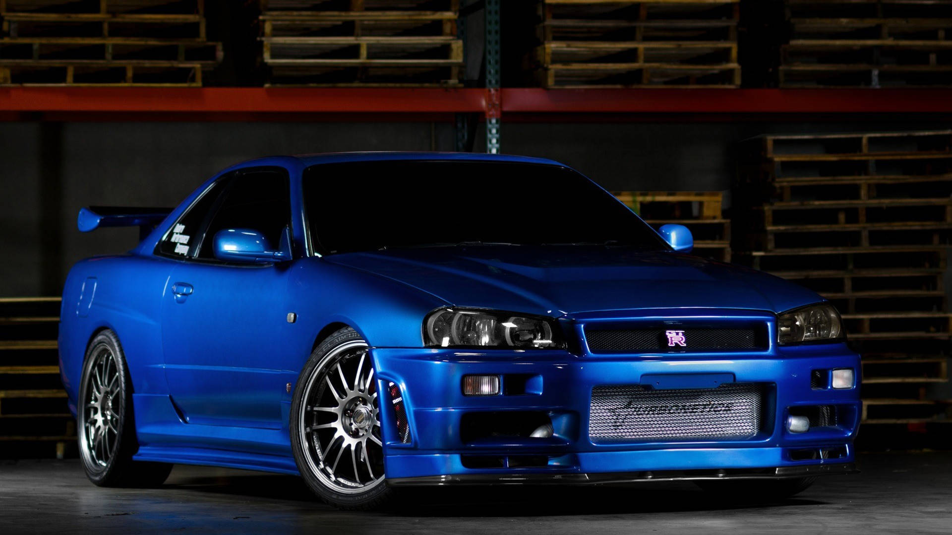 光澤藍色日產Skyline R34跑車在倉庫中，背景有木托盤。