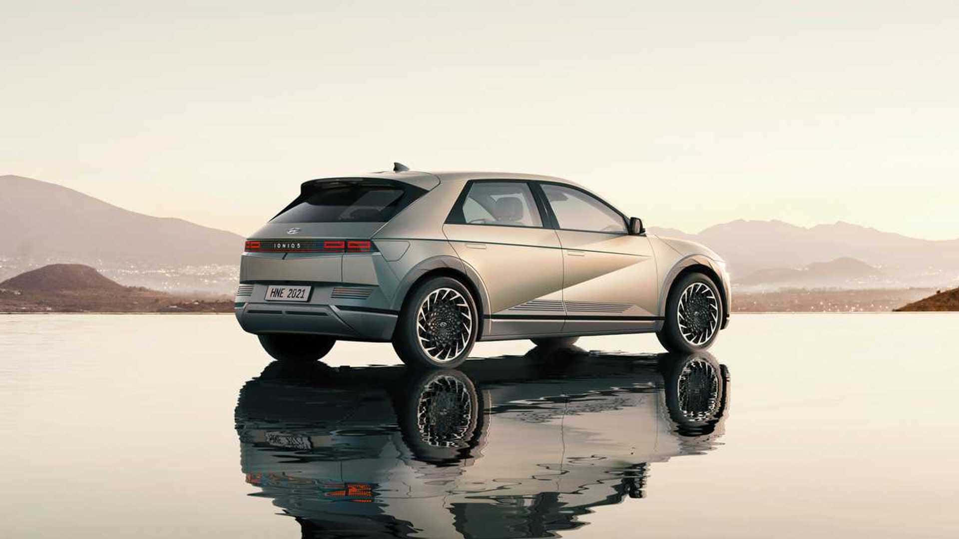 銀色電動 SUV 停在水面上，帶有山巒倒影。