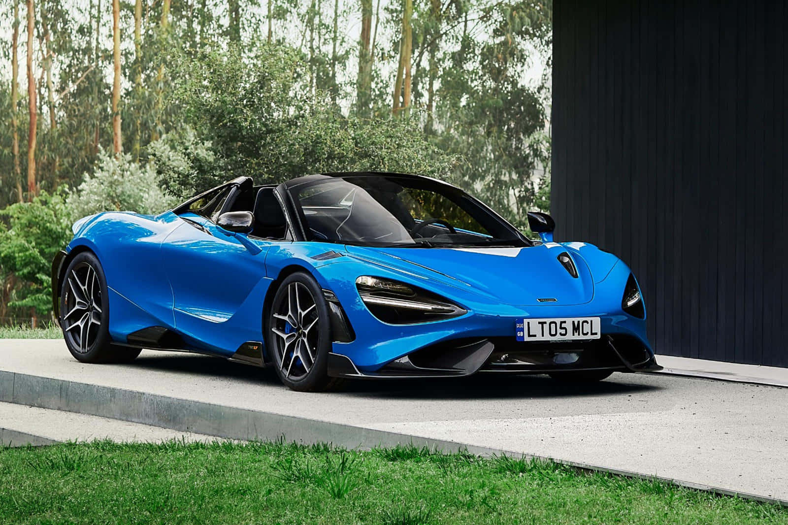 藍色McLaren 720S Spider開篷跑車停泊在戶外，靠近樹木和一座深色建築。