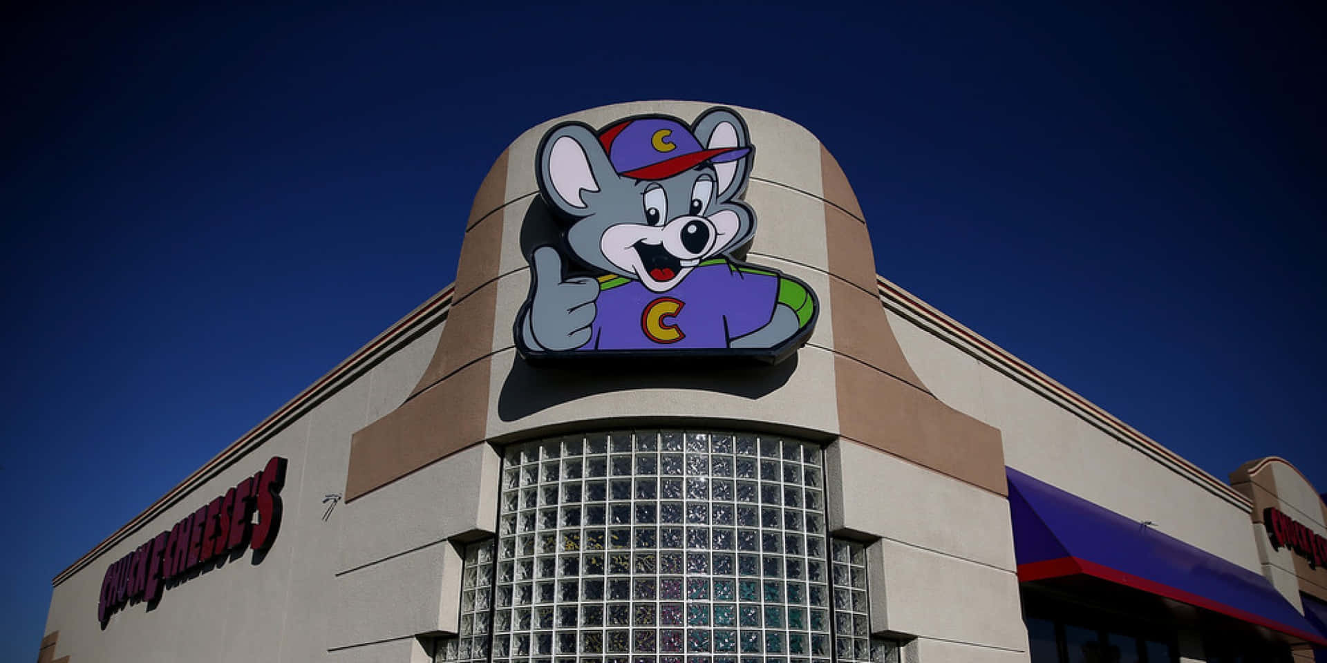 Chuck E Cheese's 吉祥物老鼠在建築物外牆豎起大拇指。