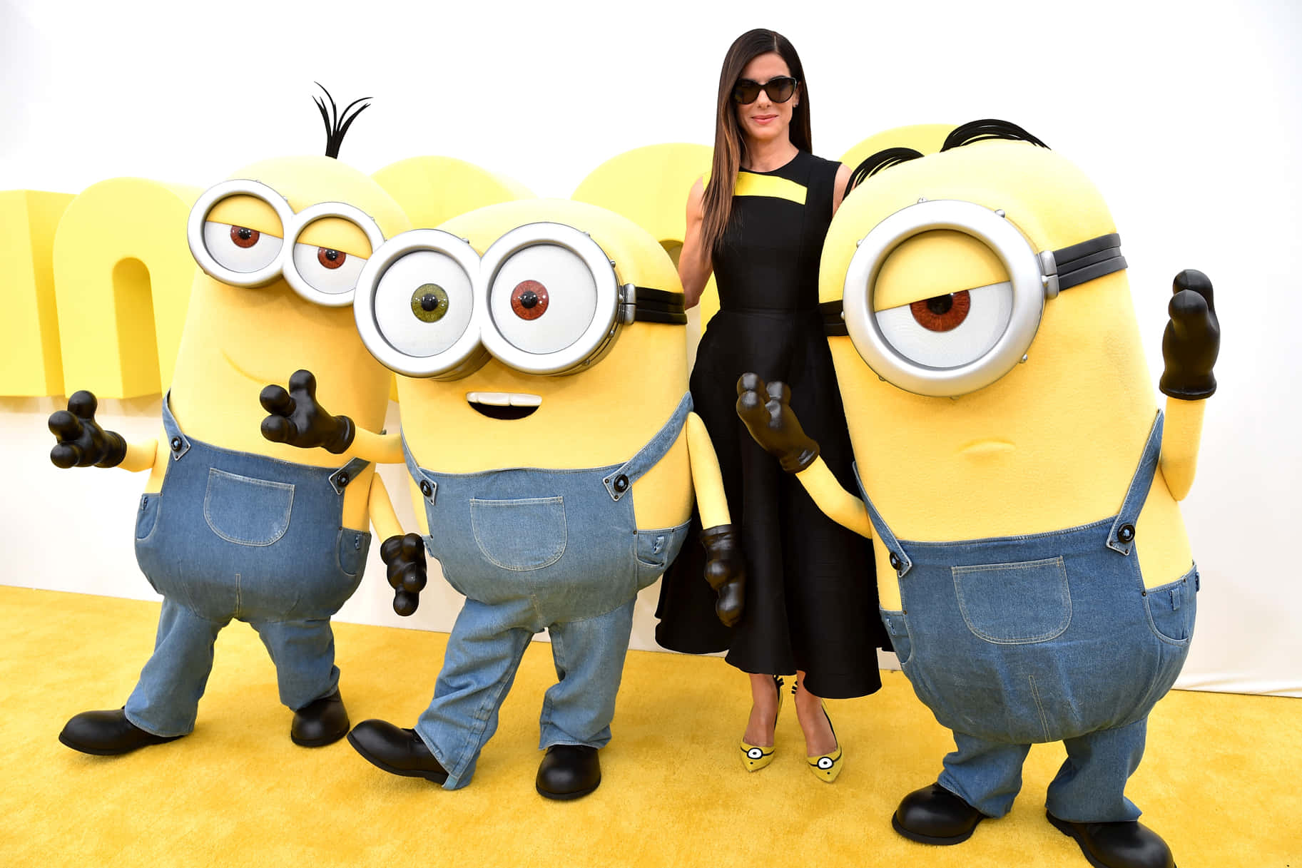 身穿黑色連衣裙的女性在活動中與三個Minion角色合影。