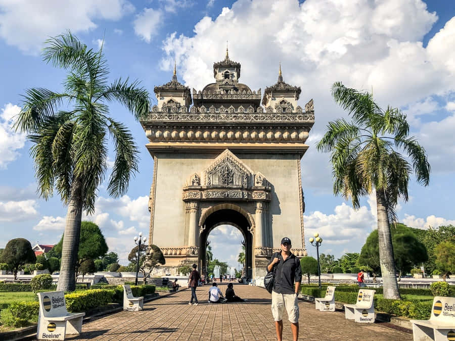 與巴特寮紀念碑的深度文化體驗 壁紙 — 一座宏偉華麗的石拱門，兩旁種有棕櫚樹，上方是明亮的藍天和蓬鬆的白雲。