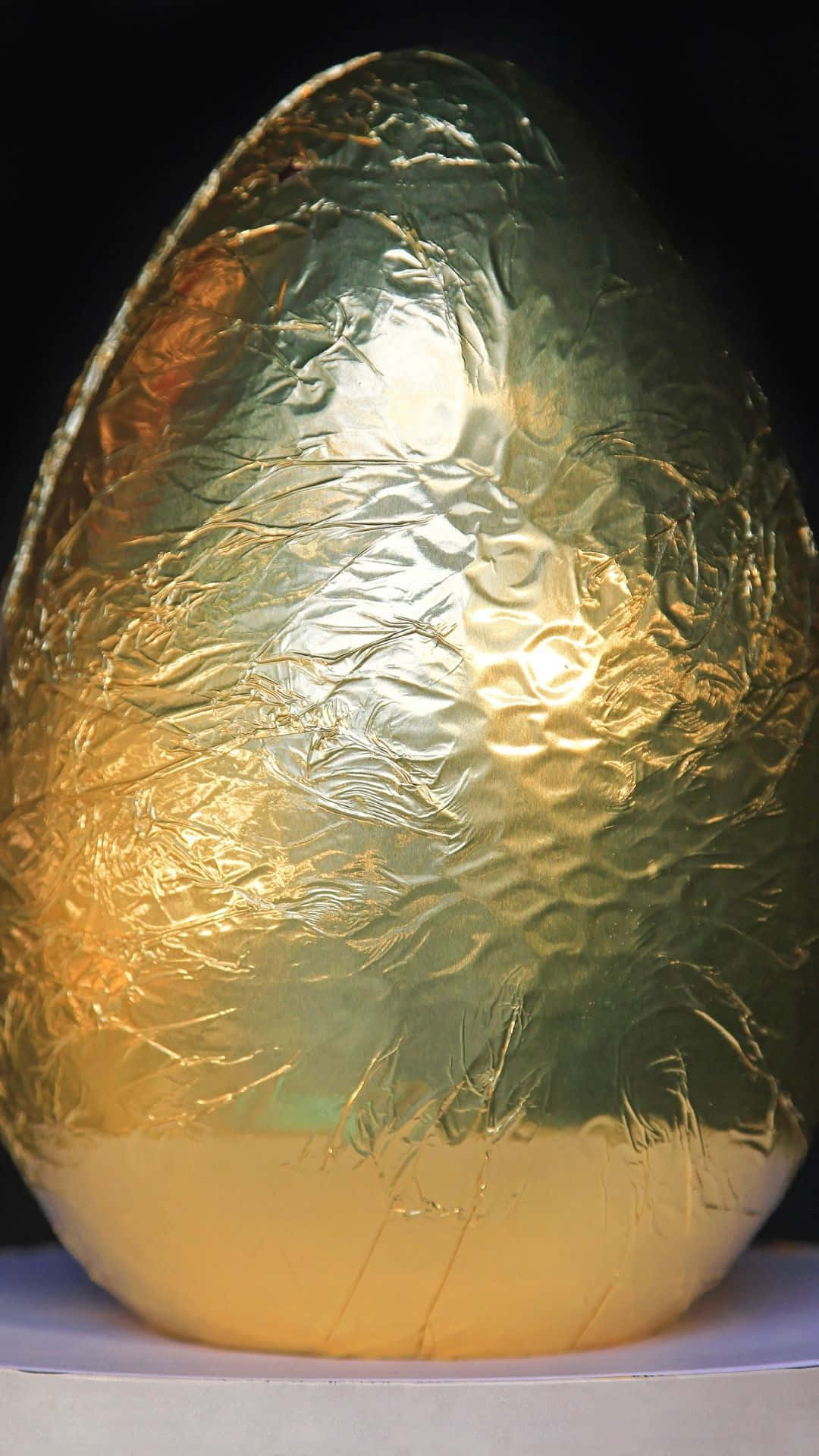 與彩蛋同樂，歡慶復活節 壁紙 — 一個大型華麗的金色箔紙包裹的蛋，帶有皺紋質感和溫暖的高光，背景為黑色。
