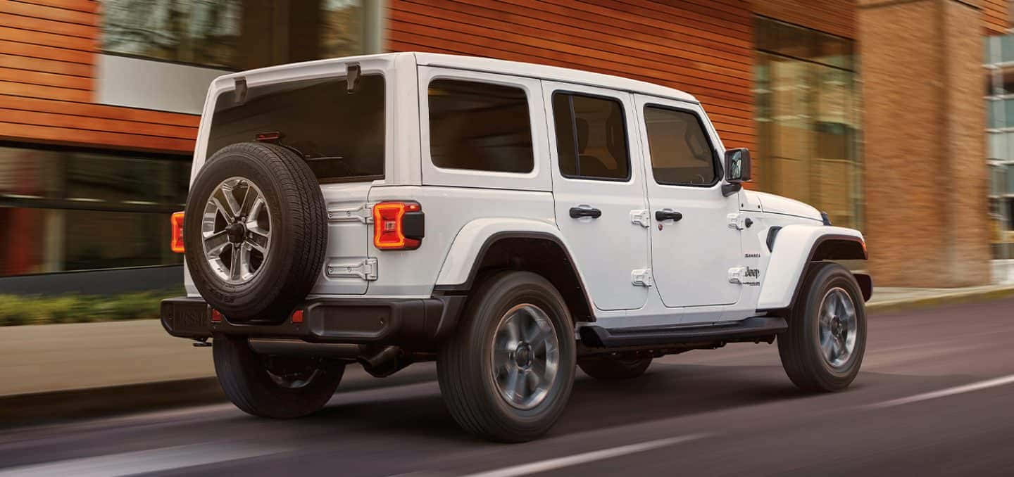 白色Jeep Wrangler在城市街道上駛過磚砌建築。