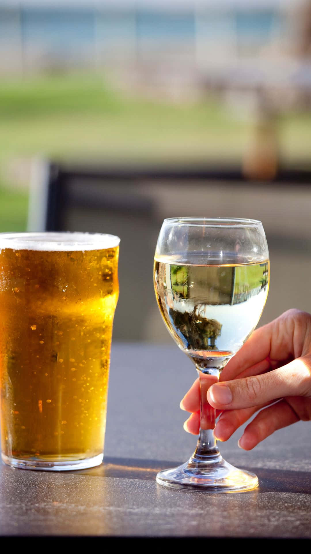 手在戶外桌子上拿著酒杯放在啤酒杯旁邊
