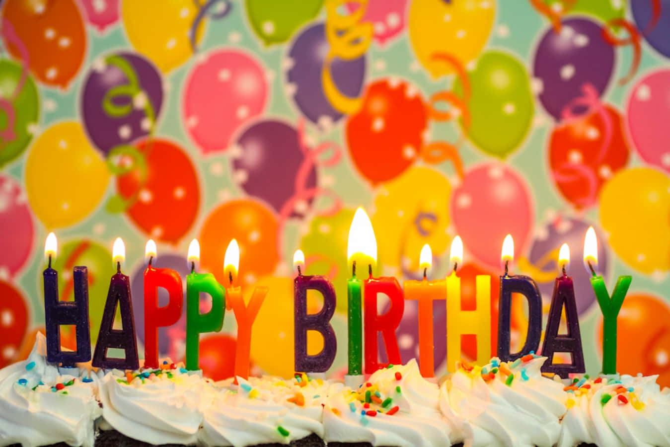 與朋友一同慶祝 壁紙 — 生日蛋糕特寫，上面有彩色字母蠟燭拼出 'HAPPY BIRTHDAY'，背景是充滿活力的氣球圖案。