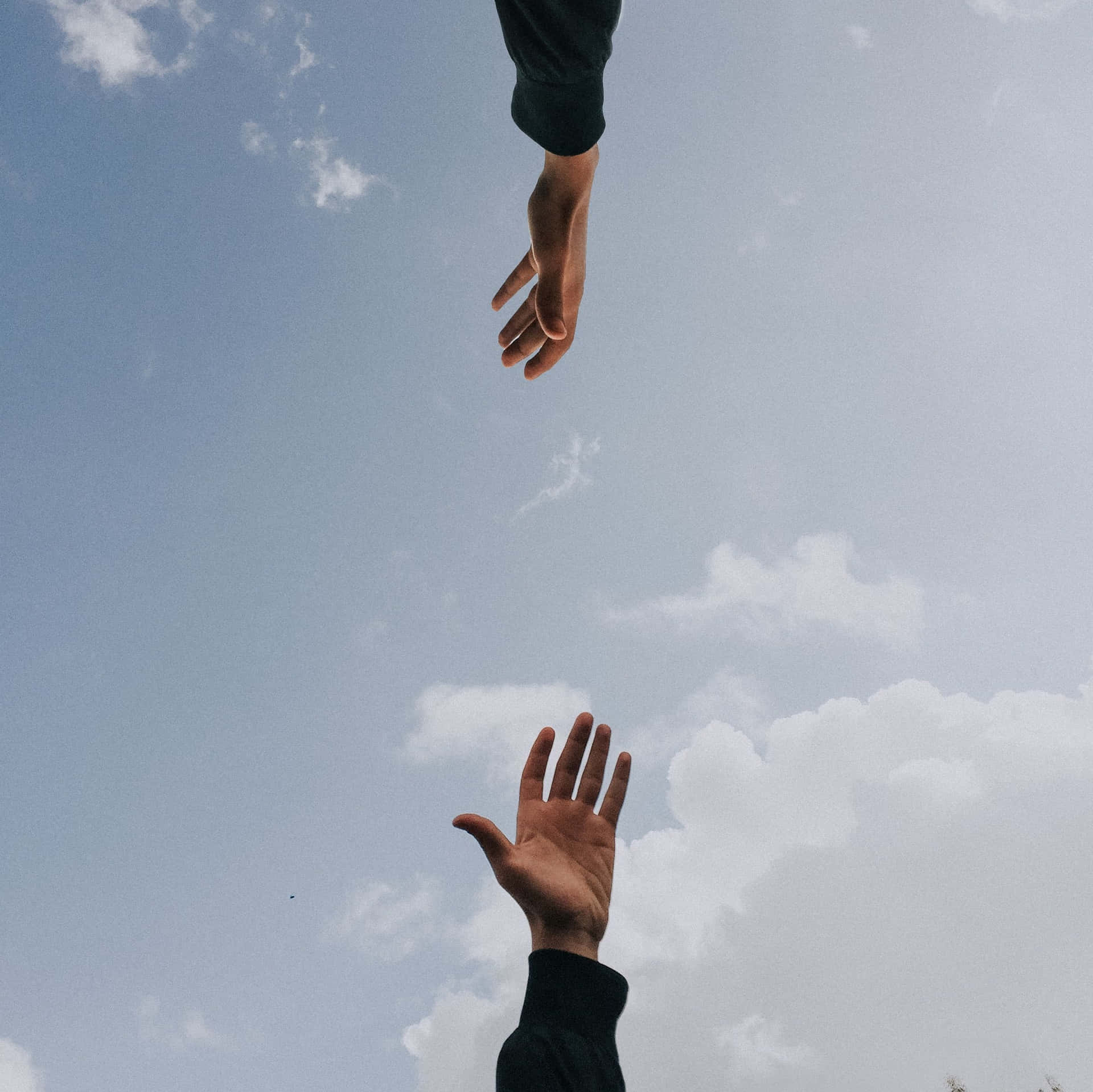 兩隻手在多雲的天空下互相伸向對方。