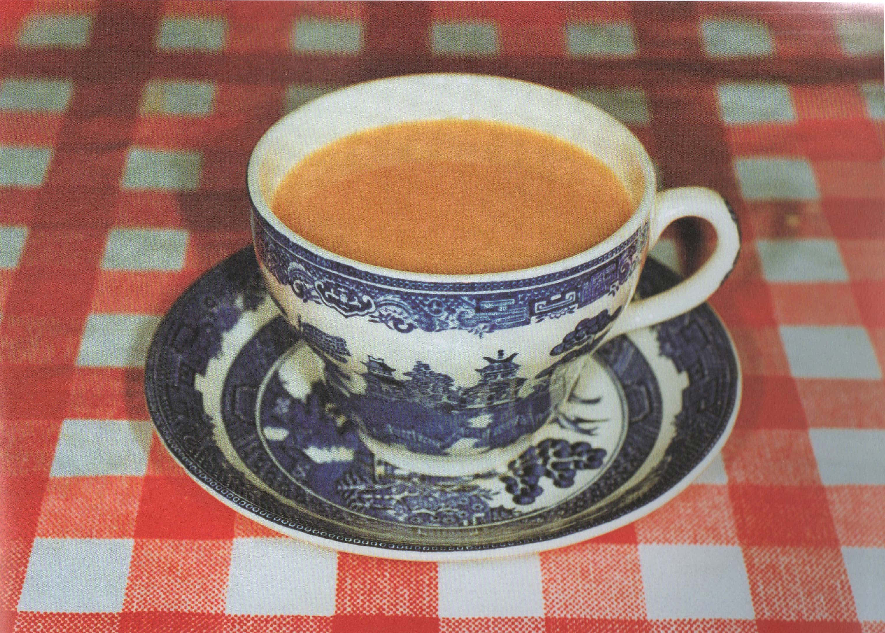 與熱茶共度寧靜時光 壁紙 — 一個藍白瓷器茶杯盛滿琥珀色茶，放在紅白格仔枱布上。