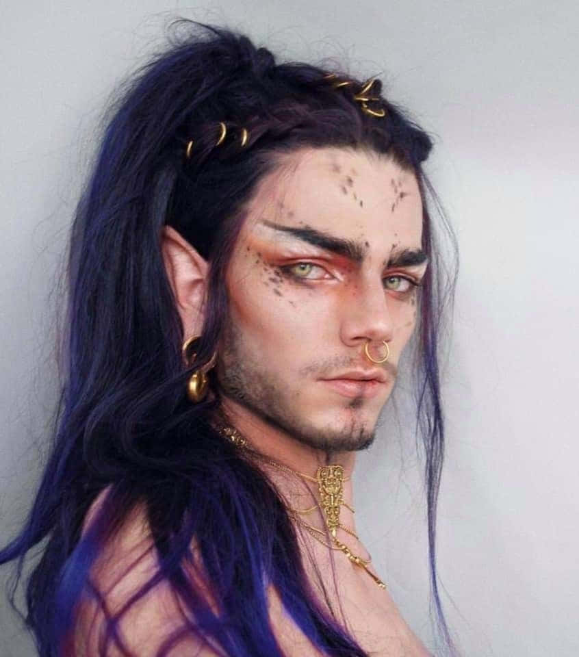 與真實精靈一同慶祝聖誕的魔法！ 壁紙 — 一個擁有深藍色長髮和金色珠寶的人，在純色背景下凝視著。