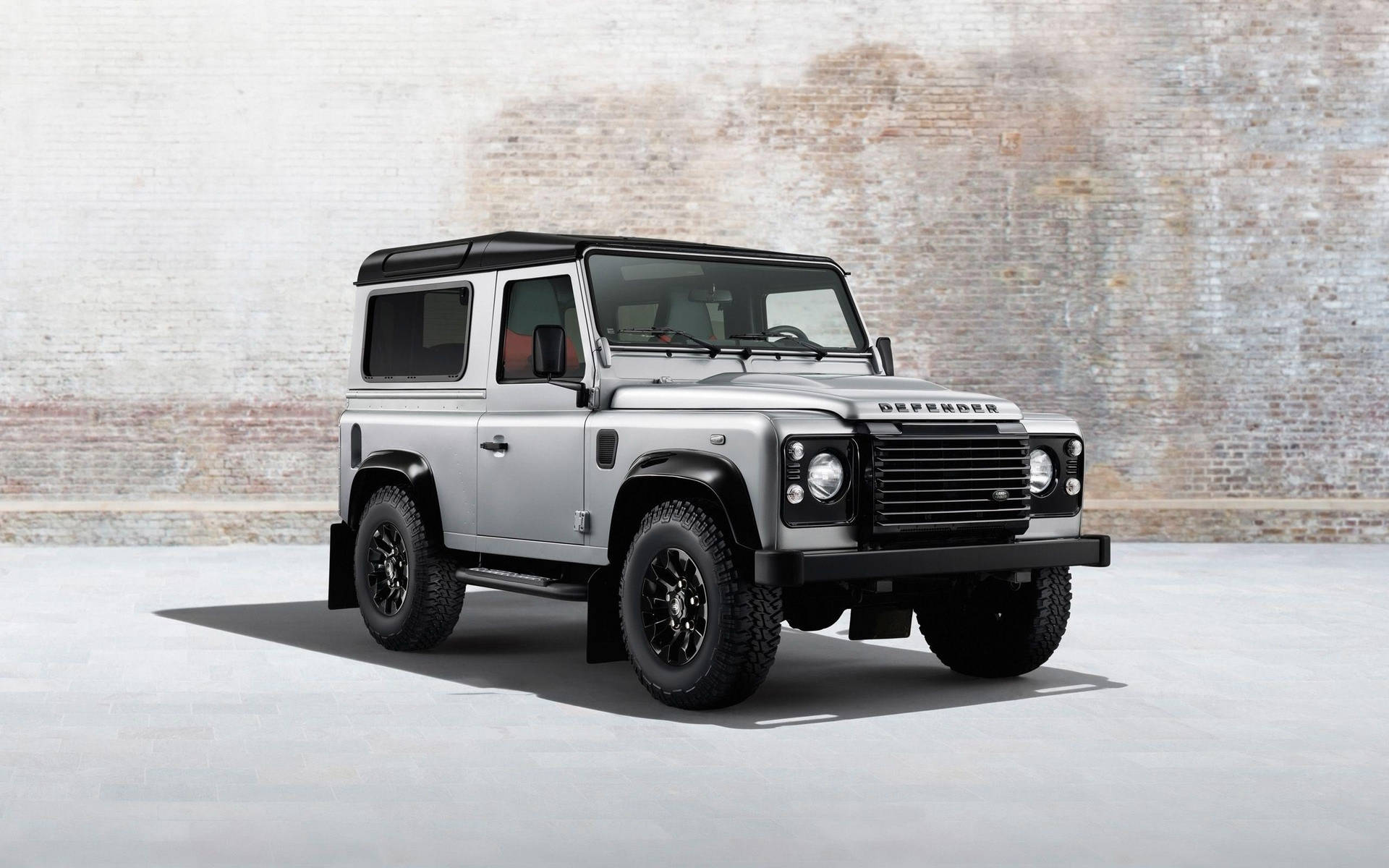 銀色 Land Rover Defender 停放在工作室的磚牆前。