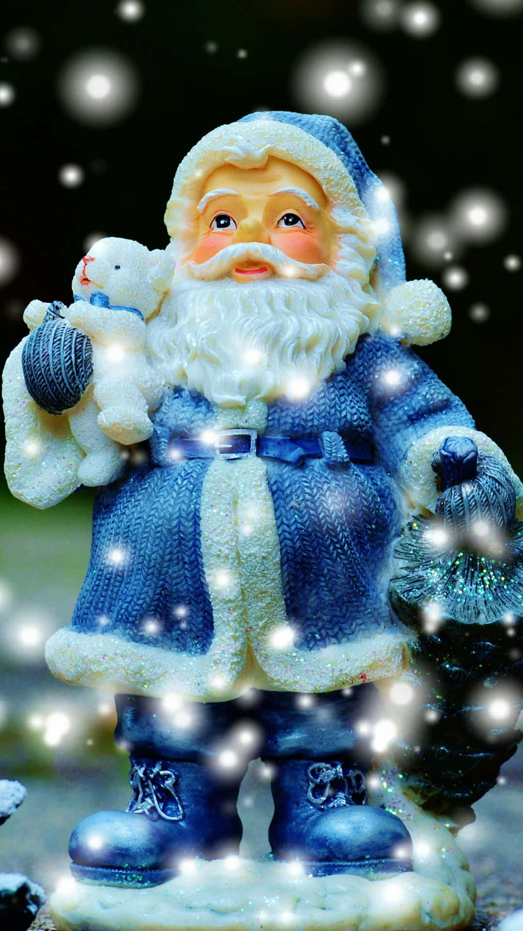藍色聖誕老人公仔在雪景中抱著泰迪熊和毛線球。