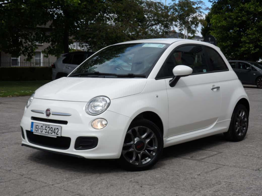 與菲亞特共度一生難忘旅程 壁紙 — 一輛純白色的Fiat 500停泊在鋪砌的停車場上，背景有綠樹和房屋，在日光下。